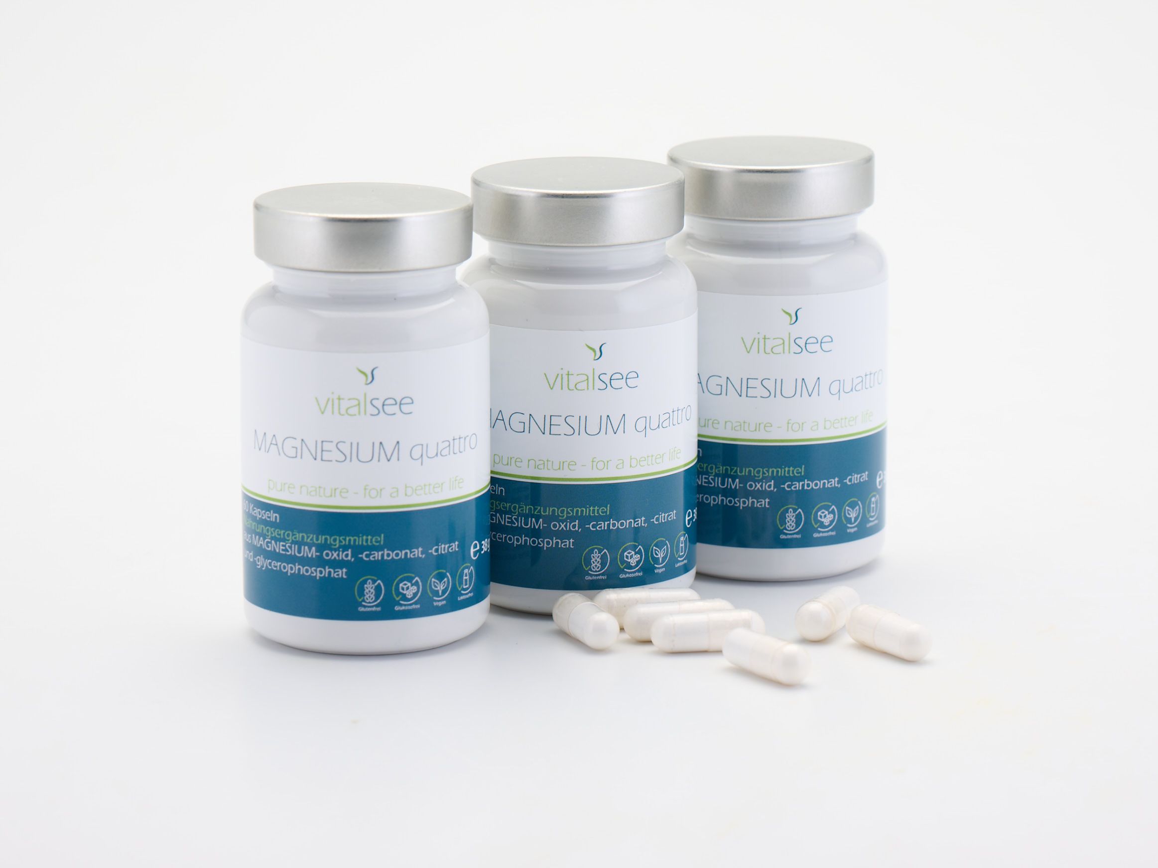 Drei weiße Flaschen mit silbernen Deckeln und Kapseln. Aufschrift: Vitalsee MAGNESIUM quattro. Blaue und weiße Etiketten.