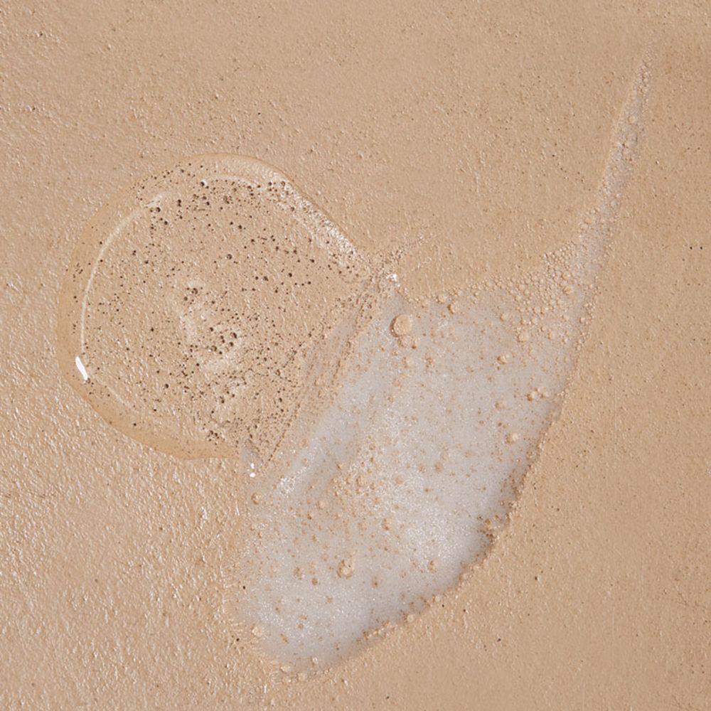 Gel-Textur auf beigem Untergrund. Runde Gel-Pfütze mit kleinen Partikeln und eine Spur. Helle Farbe.