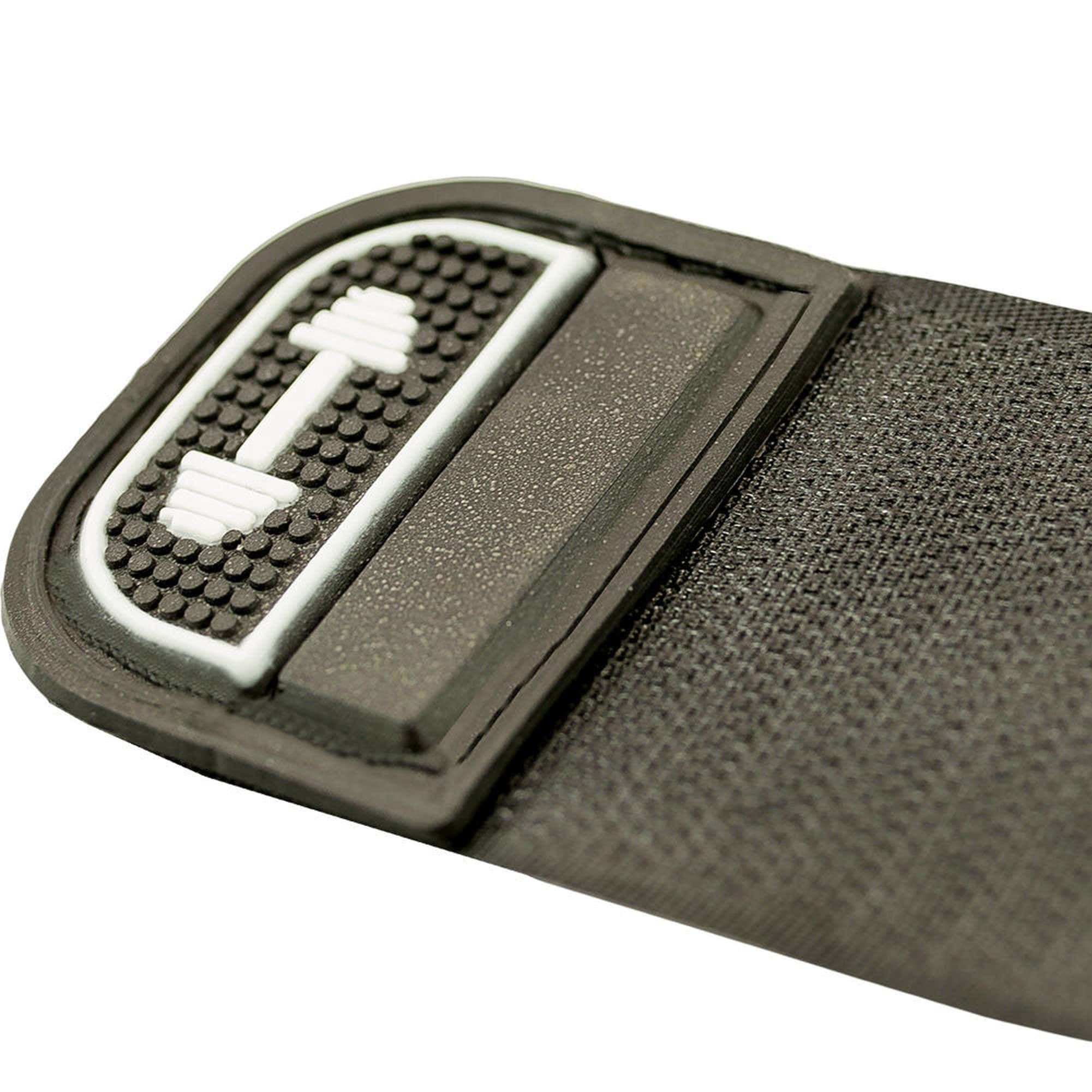 Nahaufnahme einer Handgelenkbandage. Schwarzes Textilmaterial, rechteckiges Label mit weißem Hantel-Symbol.