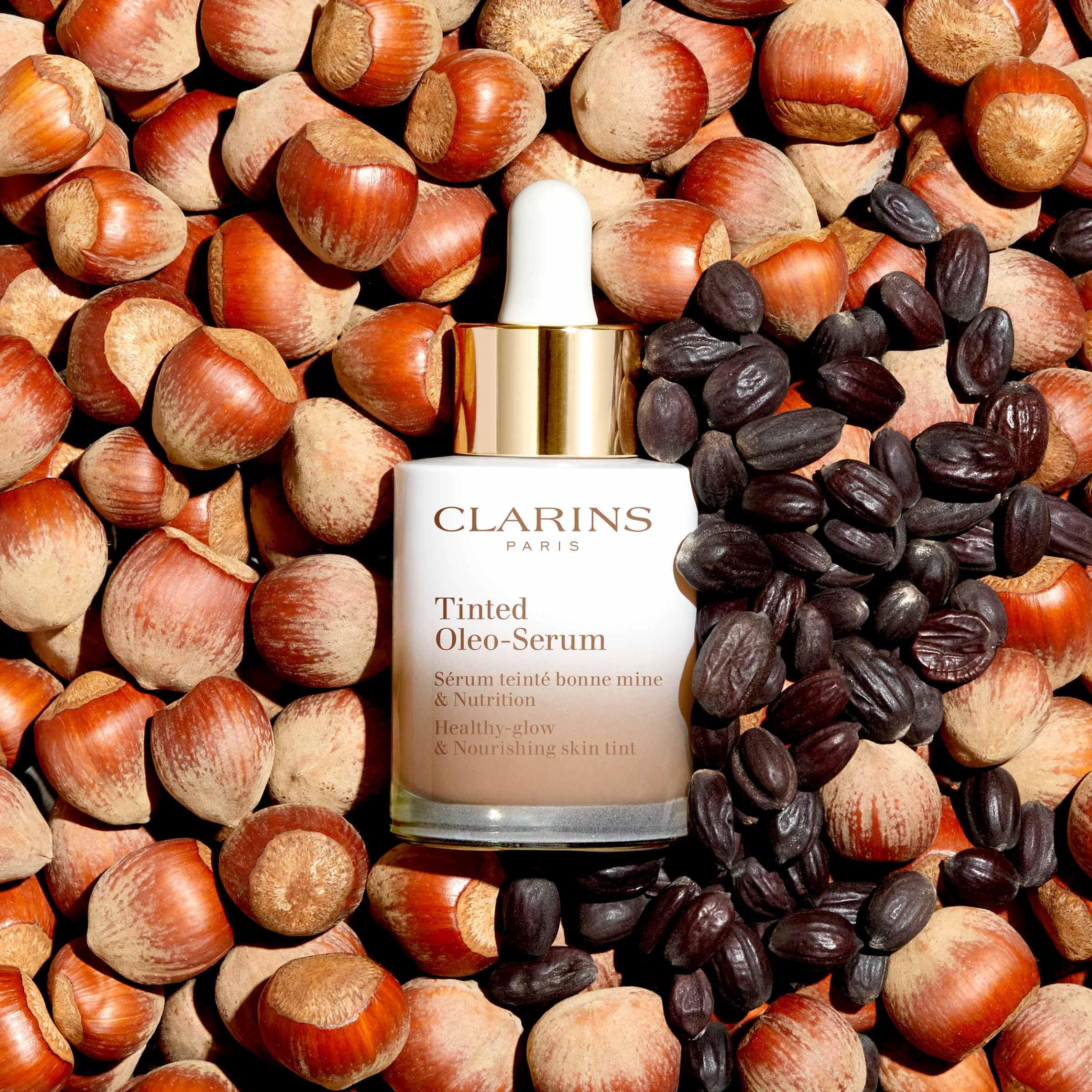 Clarins Tinted Oleo-Serum Flasche auf Haselnüssen und Samen. Weißes Glas, goldener Deckel, Produktbezeichnung.