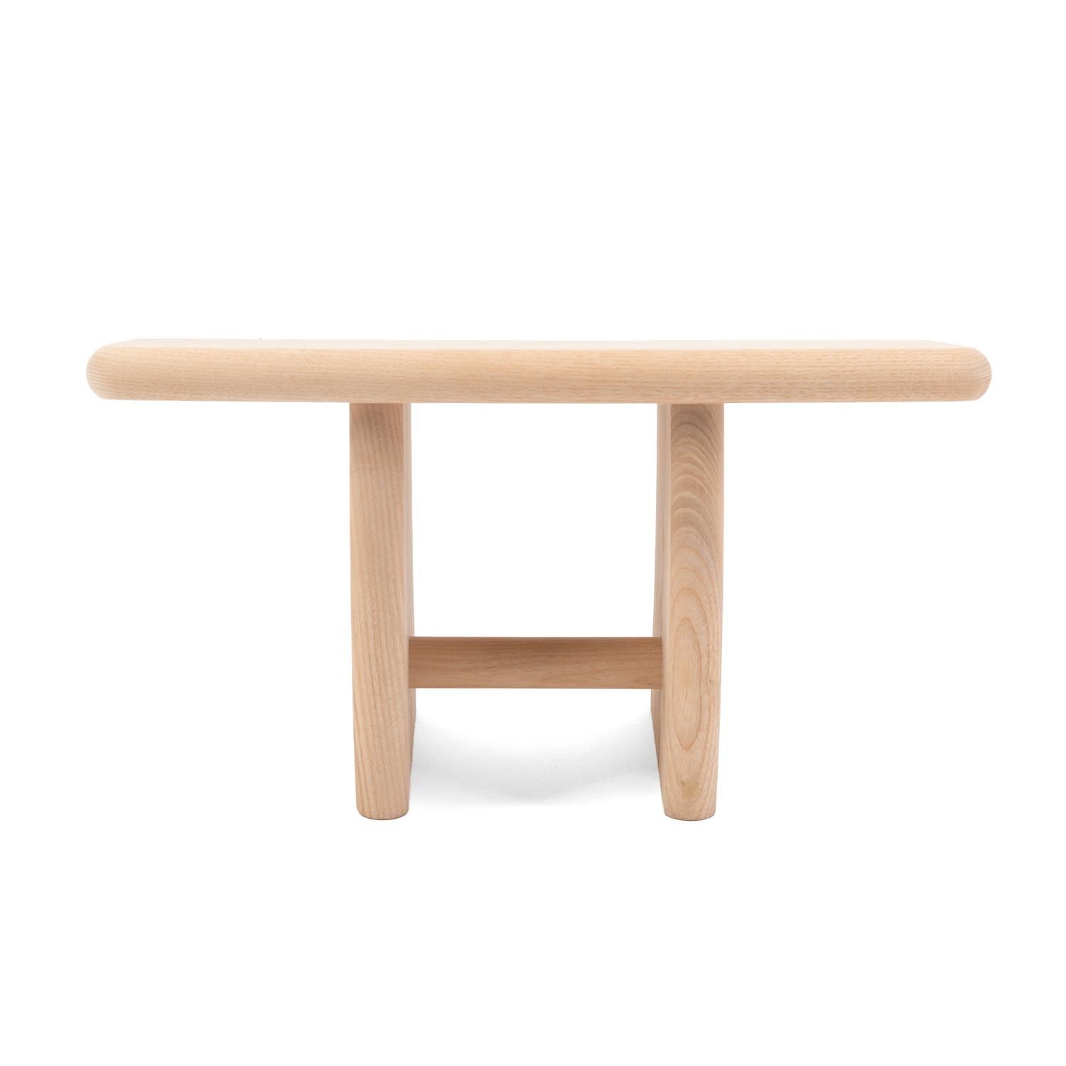 Hocker aus hellem Holz, rechteckige Sitzfläche, zwei Beine mit Querstrebe. Abgerundete Kanten.