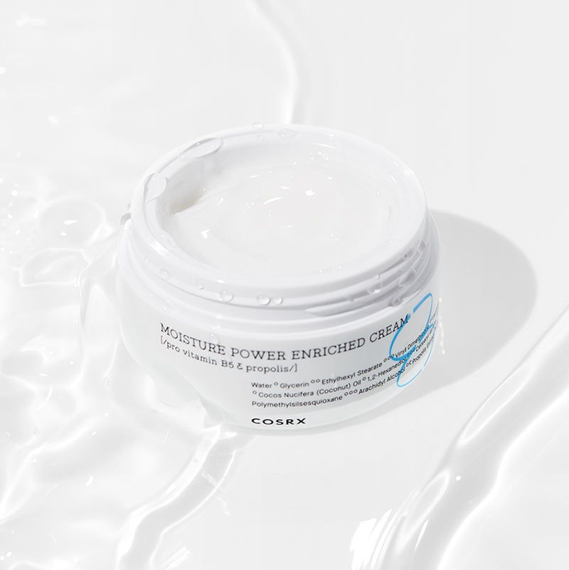 Geöffnete Creme-Dose mit Creme-Oberfläche. Aufschrift: MOISTURE POWER ENRICHED CREAM, COSRX. Wasser im Hintergrund.