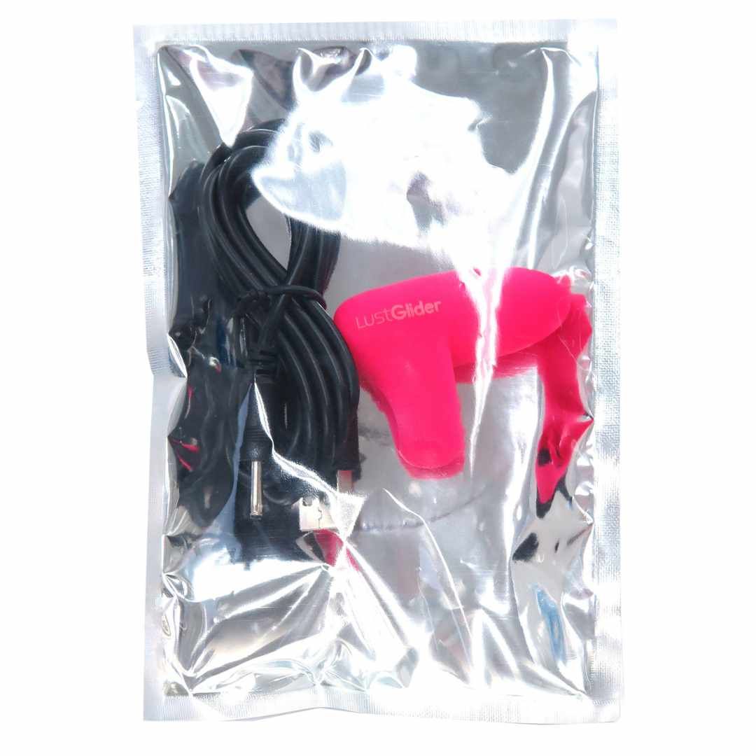 Transparente Verpackung mit rosa Finger-Vibrator, Ladekabel und Zubehör.