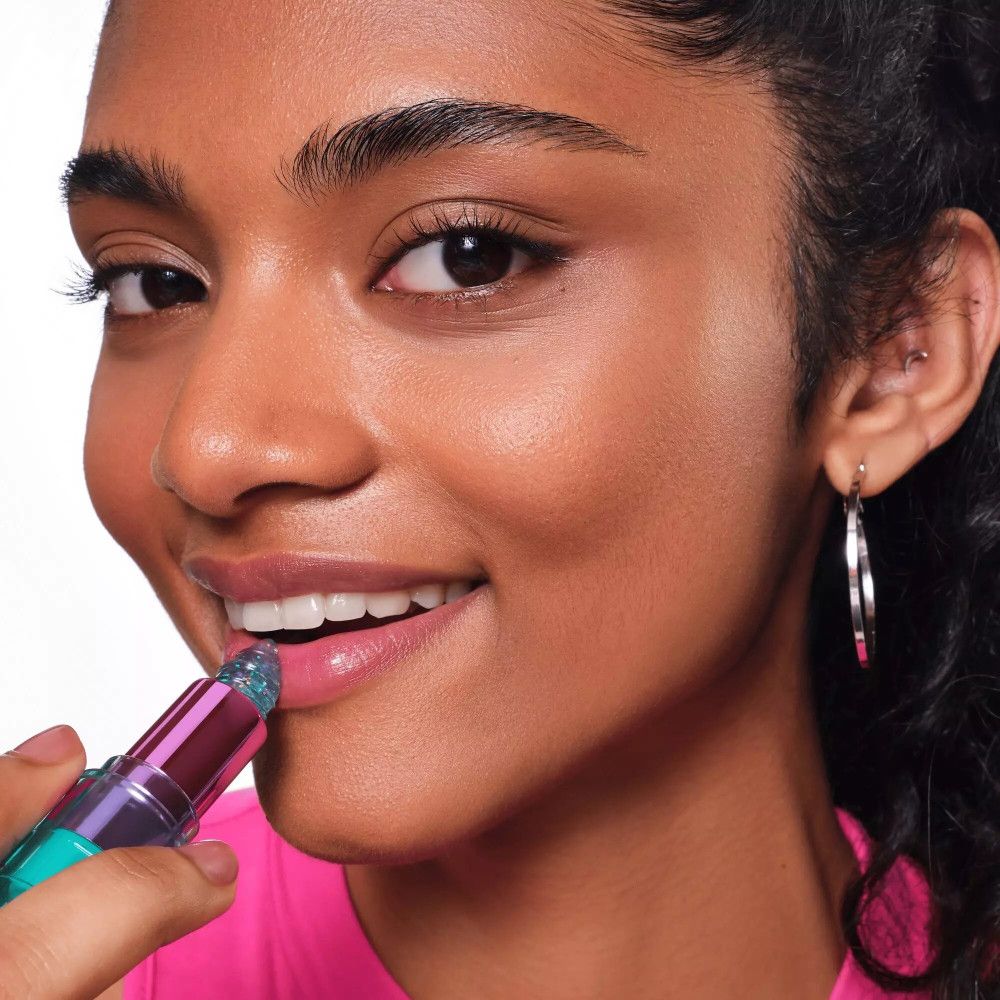 Eine Frau trägt den Aqua Jelly Lippenstift auf. Sie lächelt. Der Lippenstift ist blau und glänzend.