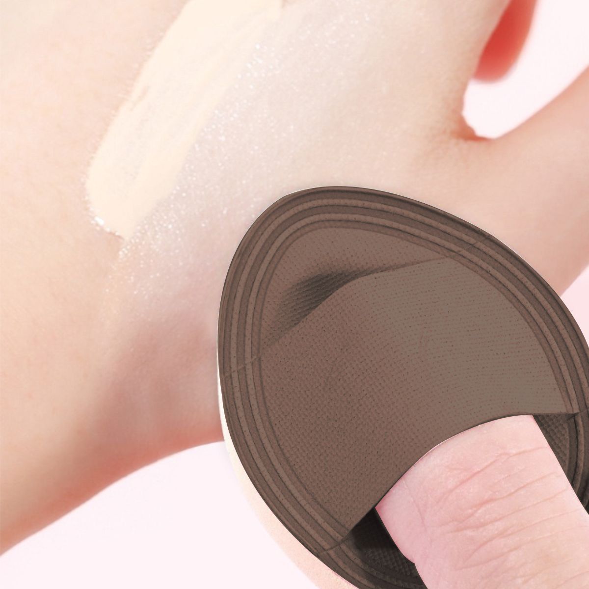 Brauner Make-up-Schwamm mit Fingerhalter auf einer Hand mit Foundation-Probe.