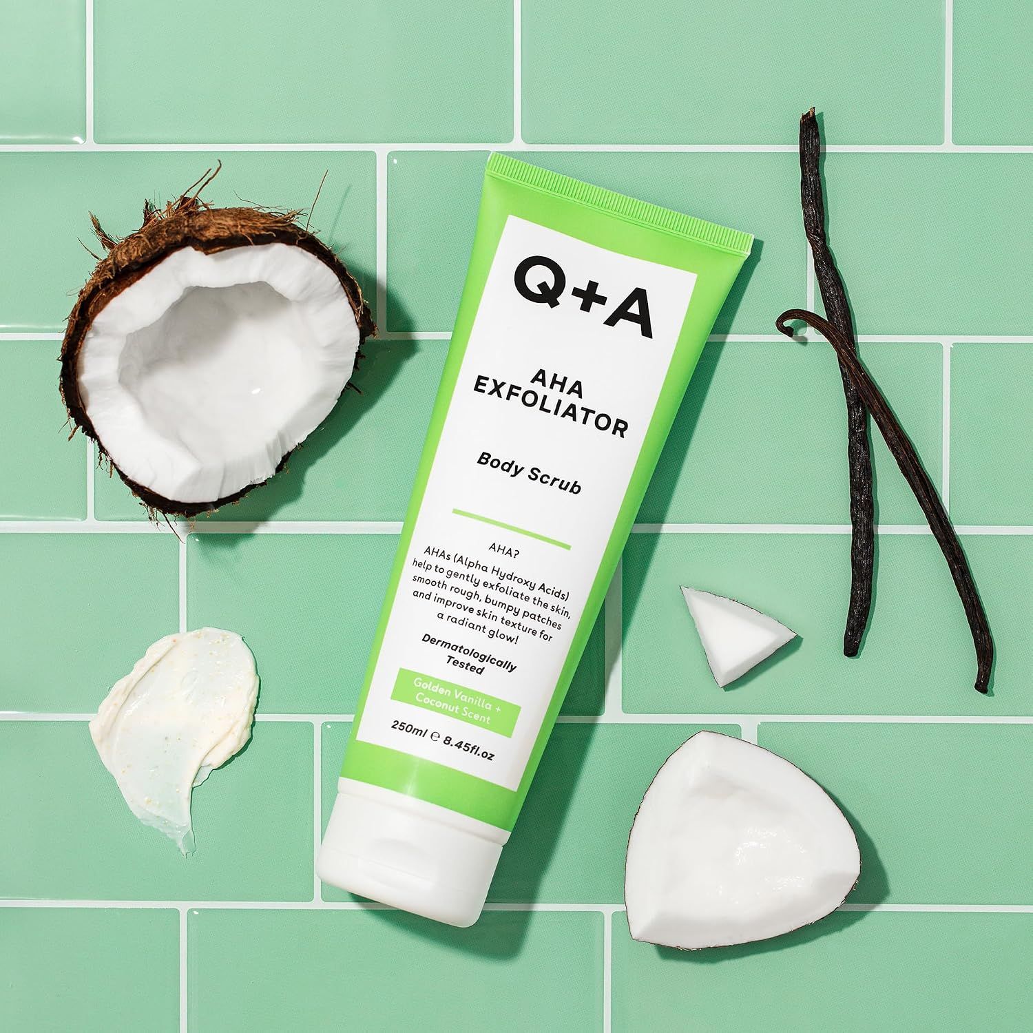 Q+A AHA Exfoliator Body Scrub in grüner Tube mit Kokosnuss und Vanilleschoten.