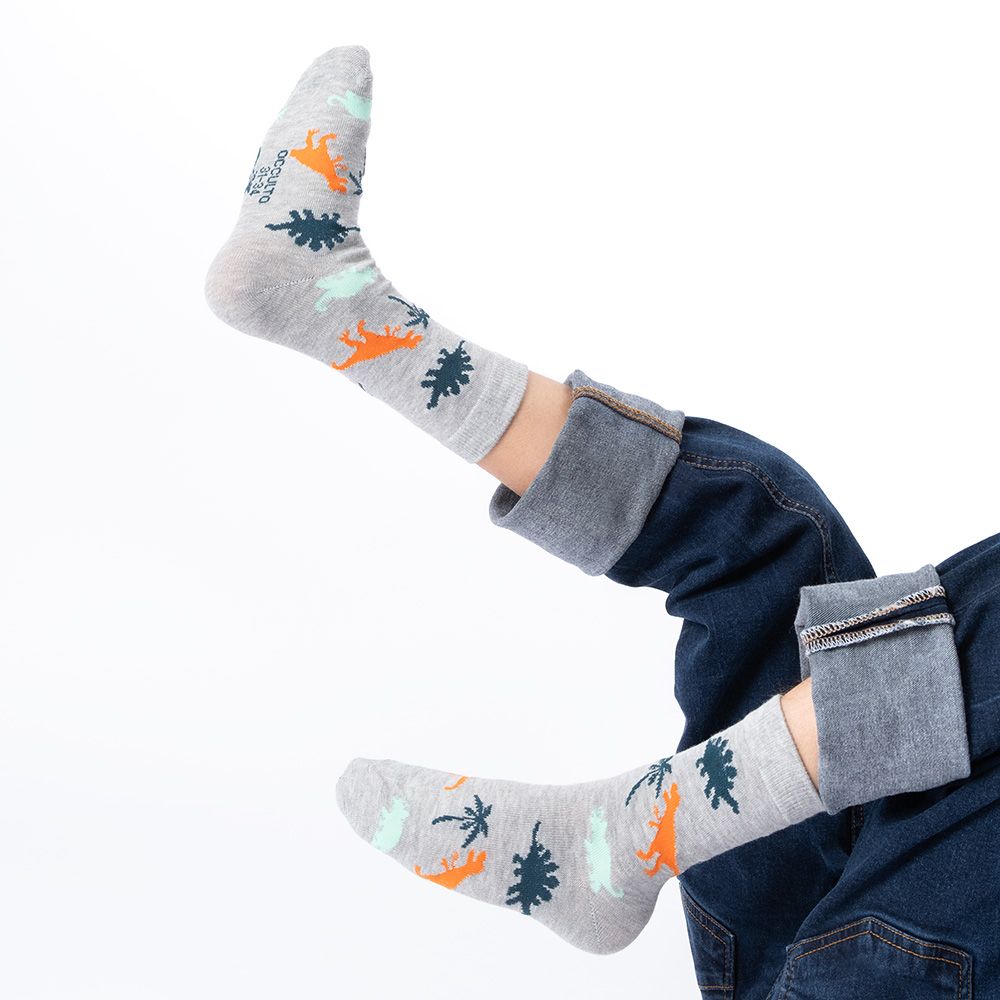 Kind trägt graue Socken mit Dinosaurier- und Palmenmotiven. Blaue Jeans. Füße in der Luft.