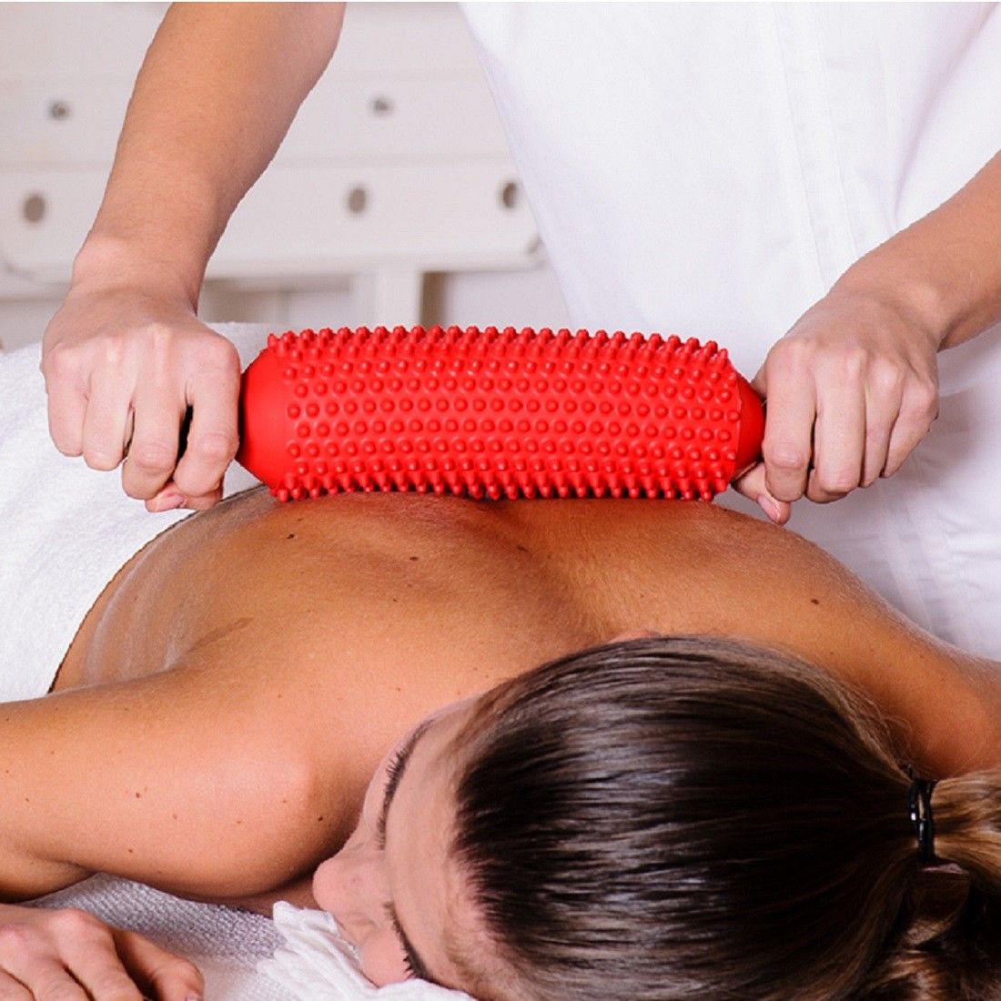 Person, die eine rote Massagerolle auf dem Rücken einer anderen Person verwendet.