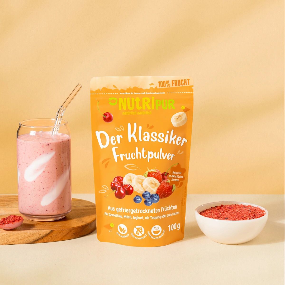 Glas mit rosa Smoothie, Strohhalm, daneben Verpackung NutriPur Fruchtpulver und Schale mit rotem Pulver. Auf einem Untersetzer.
