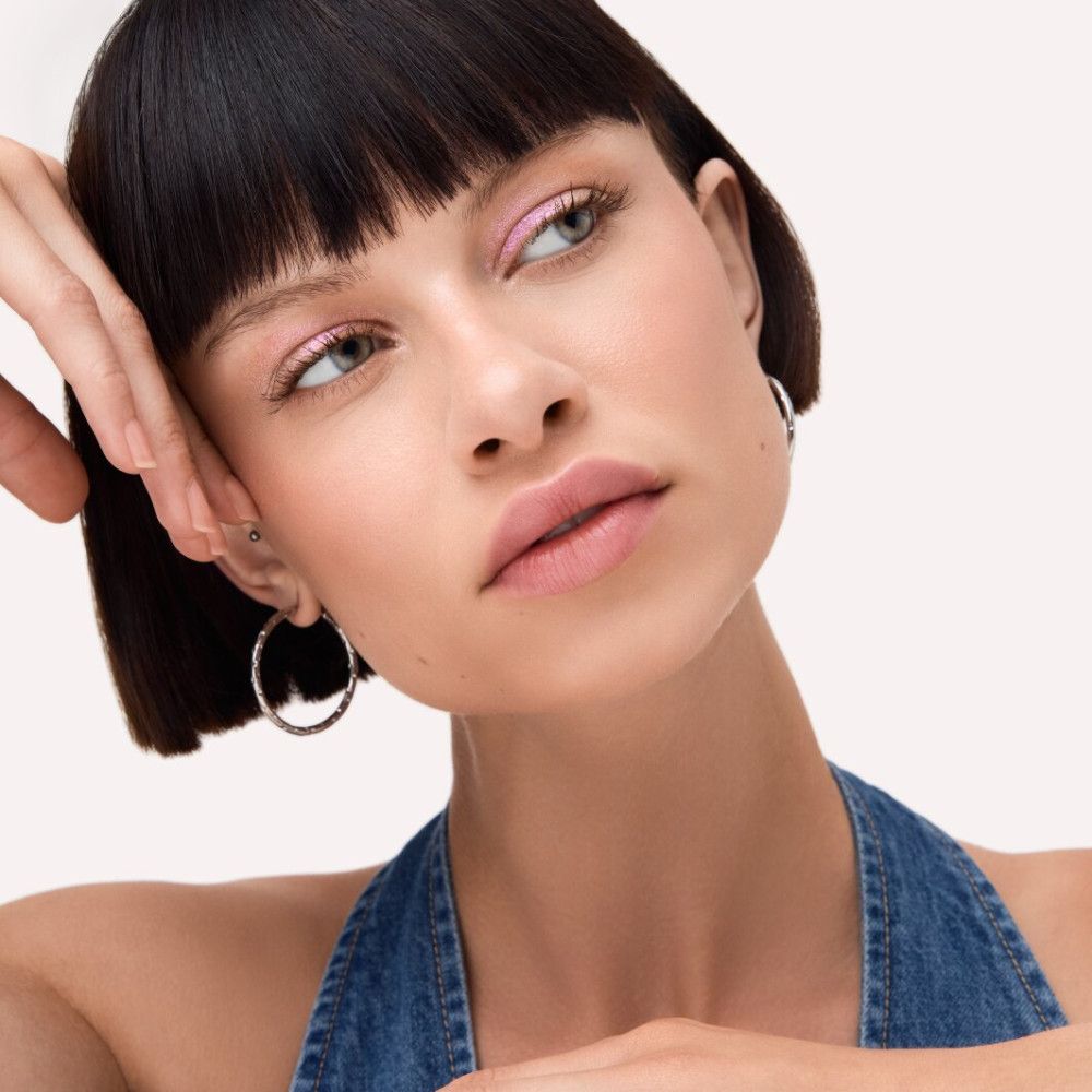Frau mit rosa Lidschatten. Sie trägt einen Jeans-Overall und silberne Creolen.