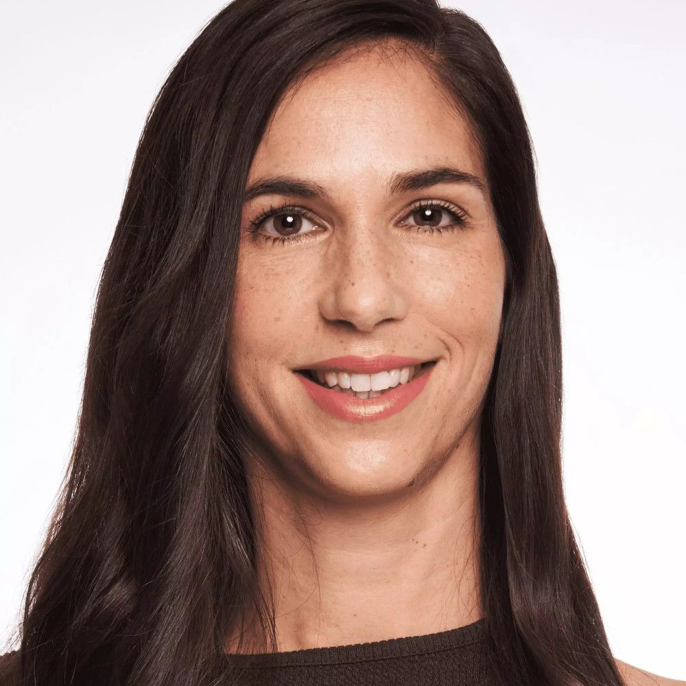 Porträt einer Frau mit langen, dunklen Haaren. Sie lächelt. Der Hintergrund ist weiß.