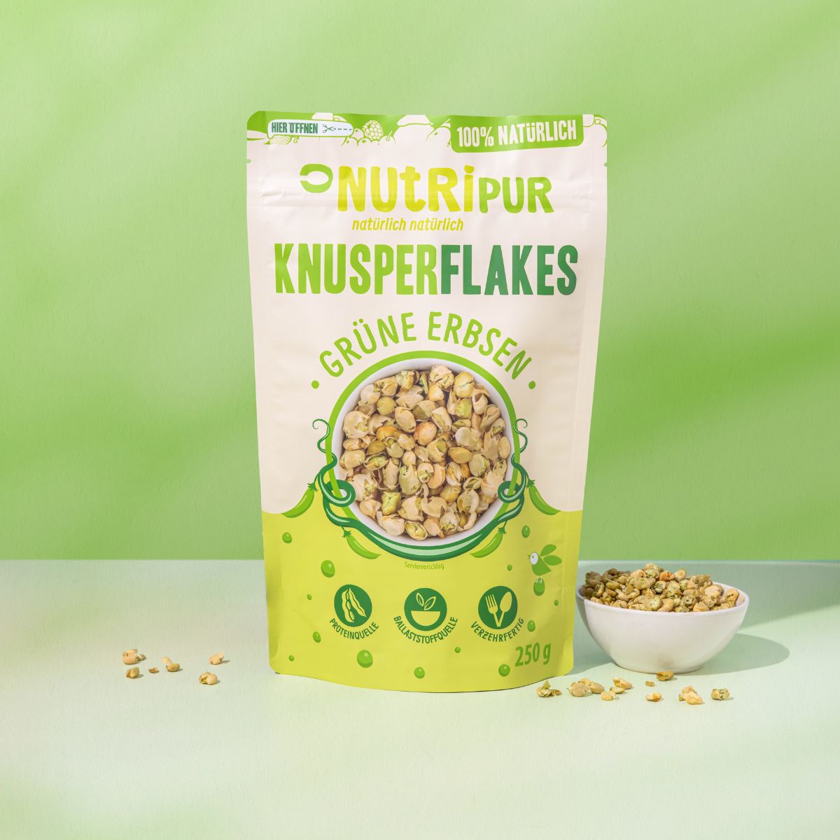Verpackung von NutriPur Grüne Erbsen Knusperflakes. Aufschrift: Knusperflakes, Grüne Erbsen, 250g. Eine Schale mit Flakes daneben.