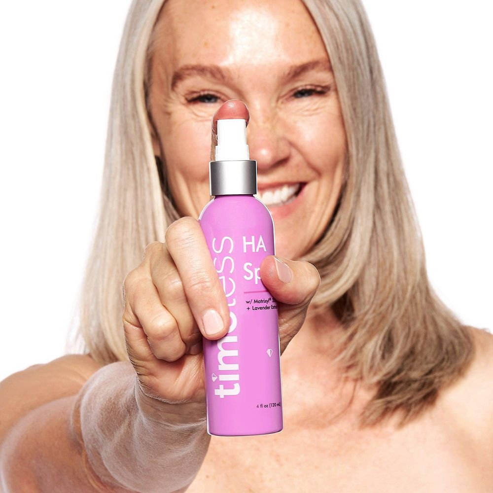Frau hält rosa Sprühflasche. Beschriftung: timeless, HA Spray, Matrixyl 3000, Lavendelextrakt. Flasche mit Sprühkopf.