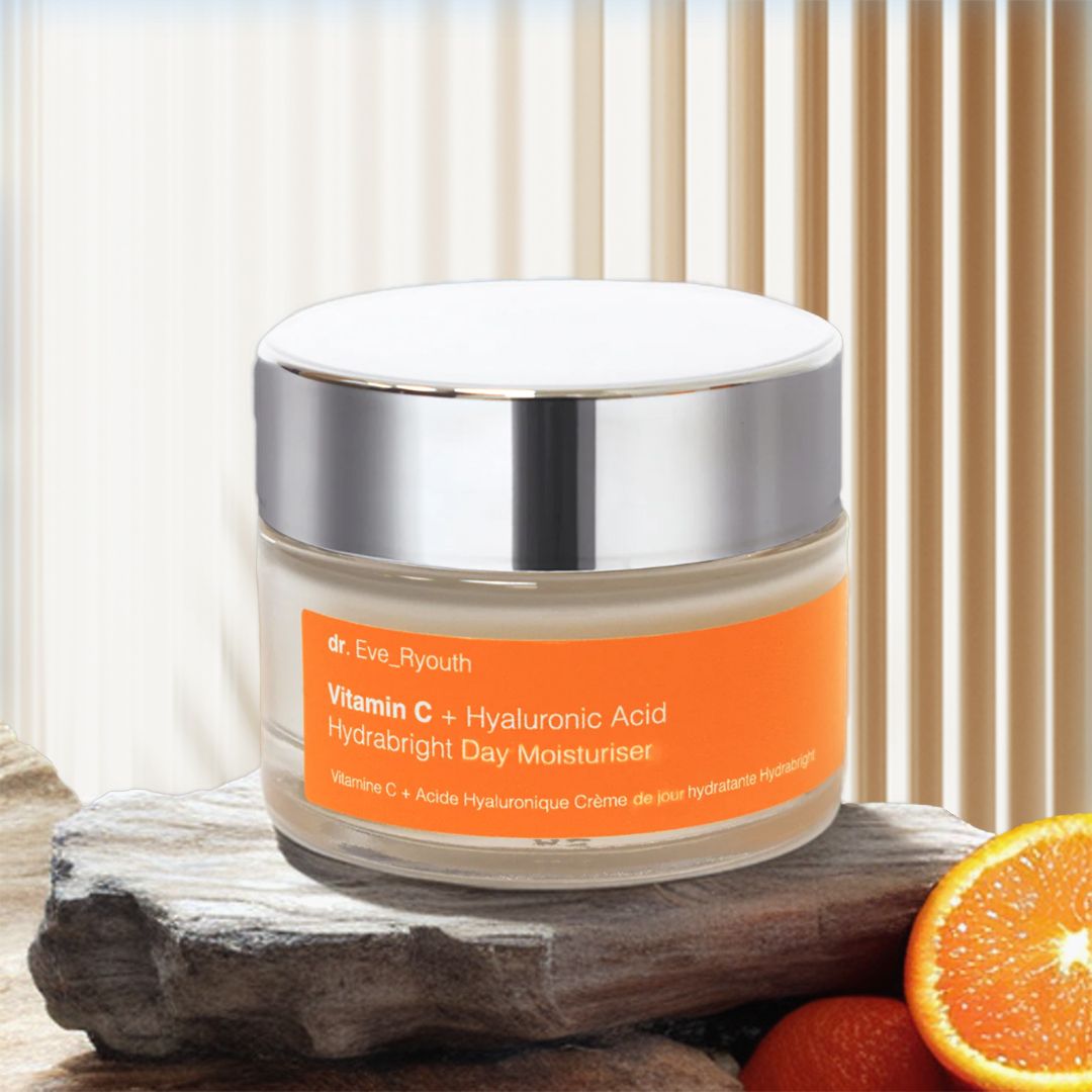 Creme-Tiegel mit silbernem Deckel. Aufschrift: Vitamin C + Hyaluronsäure Hydrabright Day Moisturiser. Auf Stein und Orange.