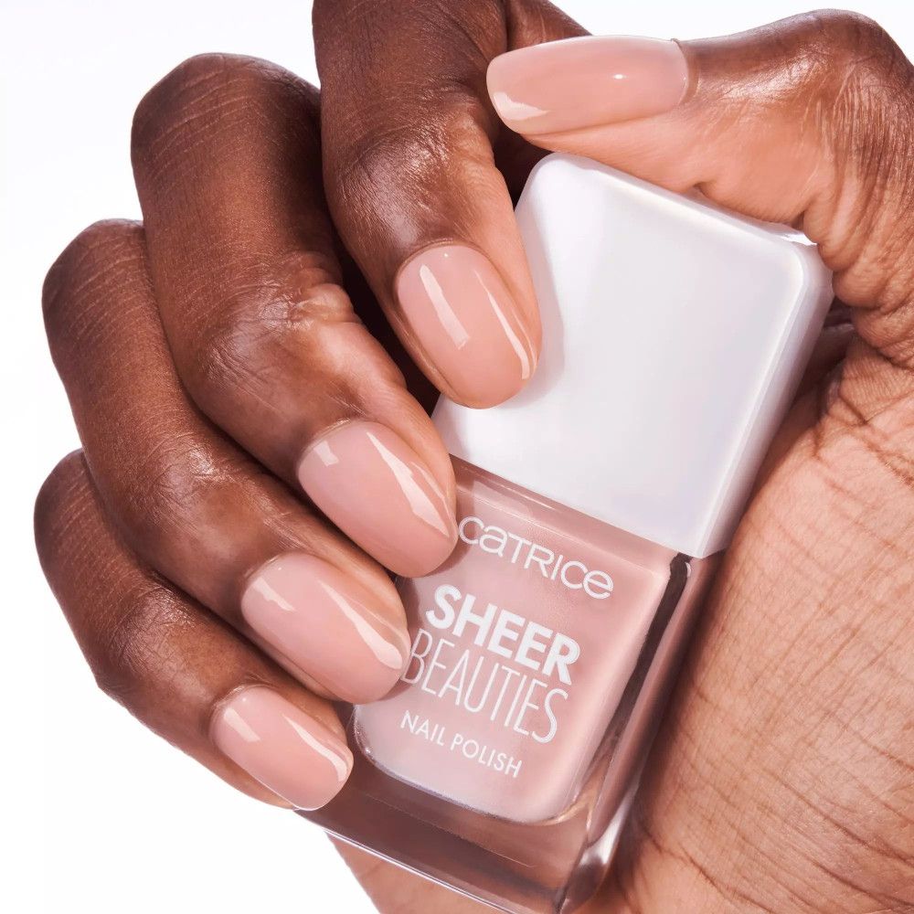 Hand mit lackierten Nägeln und Nagellackflasche. Aufschrift: CATRICE SHEER BEAUTIES NAIL POLISH.