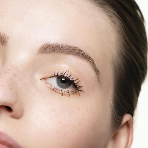 Nahaufnahme eines Auges mit getuschten Wimpern. Augenbraue und Haut sind sichtbar.