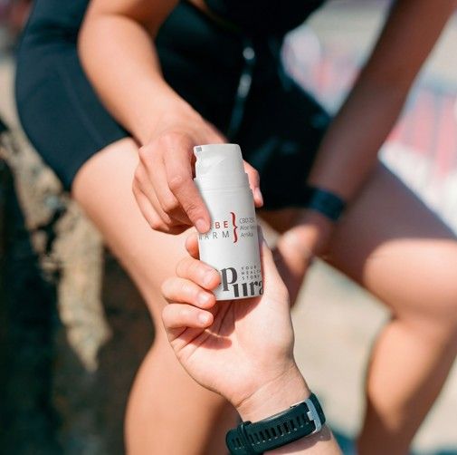 Zwei Hände halten eine weiße Salbenflasche mit CBD 250, Aloe Vera, Arnika. Produkt im Freien.