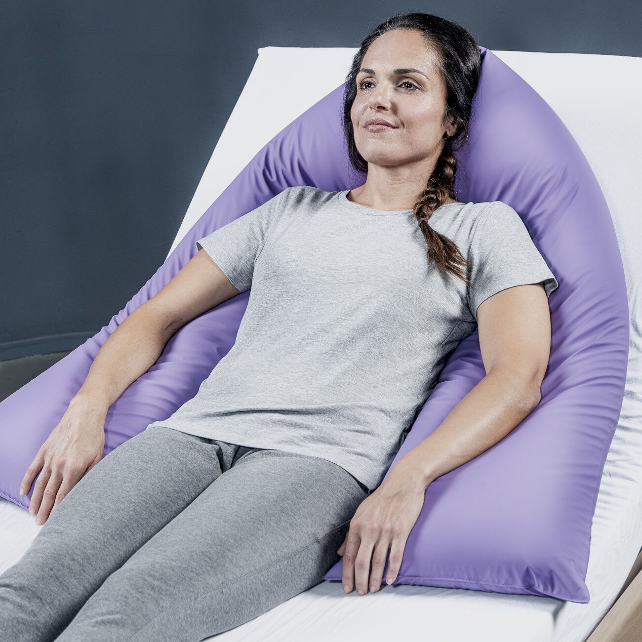 Eine Frau liegt auf einem Bett und wird von einem lila KUBIVENT PurplePos VariMed Positionierungskissen gestützt. Das Kissen ist U-förmig.