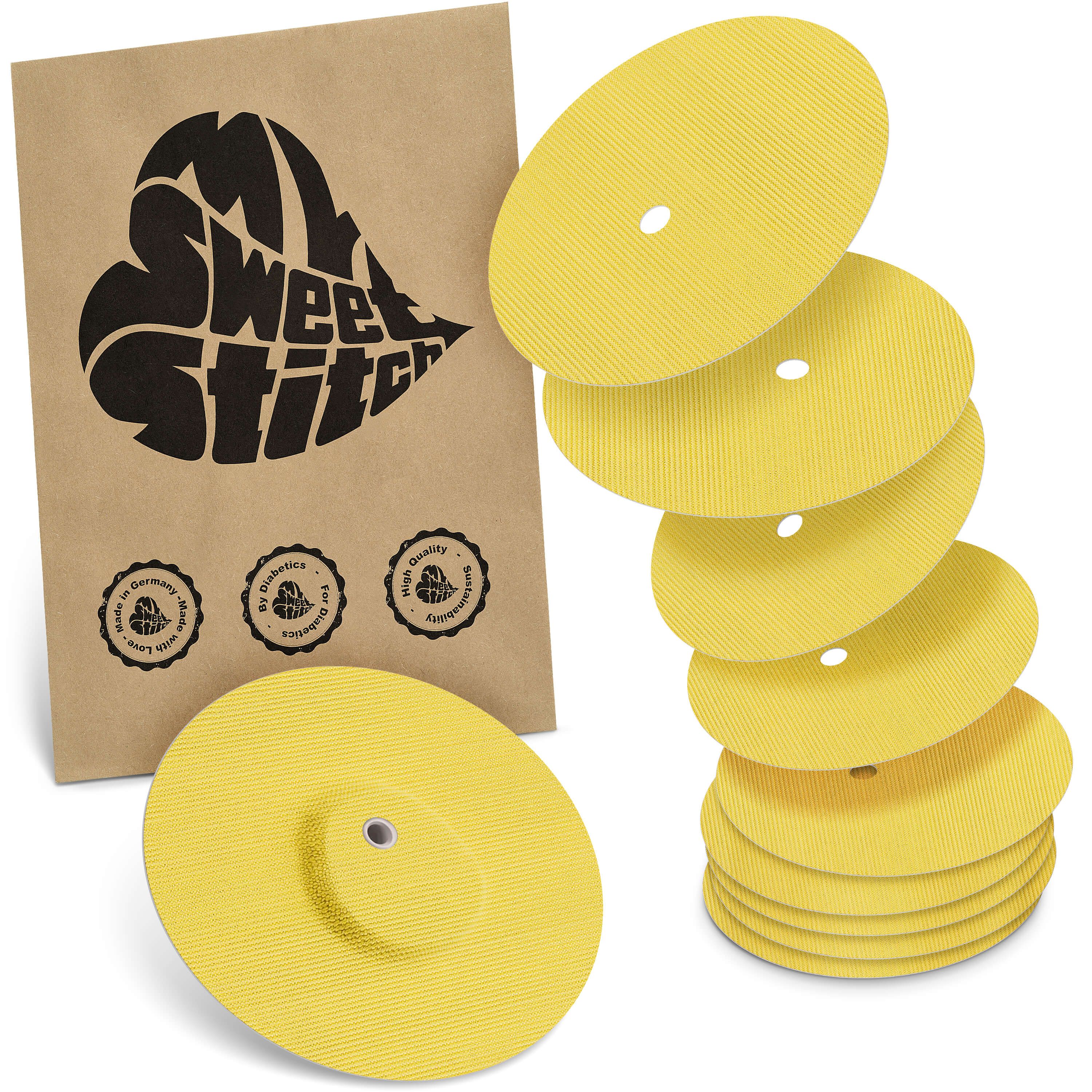 Gelbe, runde Pflaster mit Loch, teilweise gestapelt. Braune Verpackung mit Logo und Qualitätssiegeln.