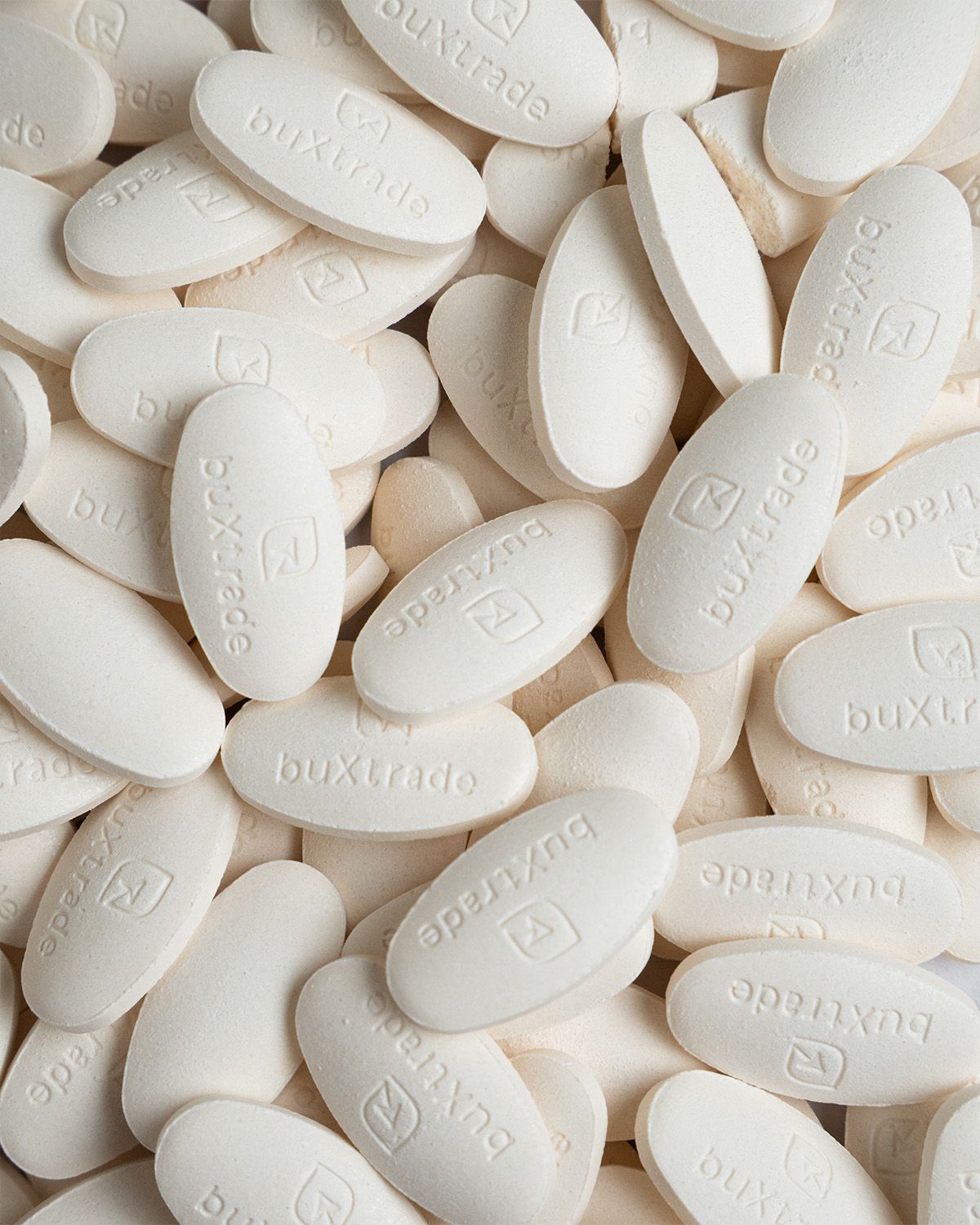 Nahaufnahme von vielen weißen, ovalen buXtrade Vitamin C Tabletten, die sich überlappen.