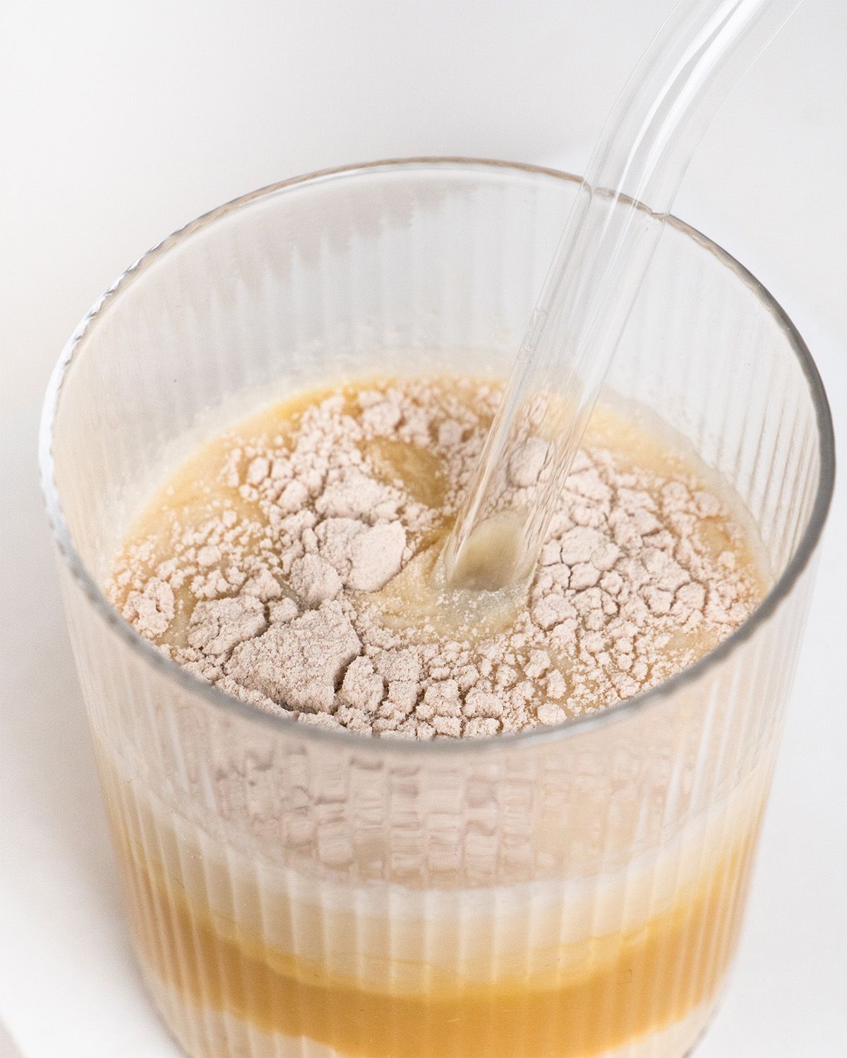 Glas mit Flüssigkeit und Flohsamenschalenpulver. Pulver wird mit einem Strohhalm in Flüssigkeit eingerührt.