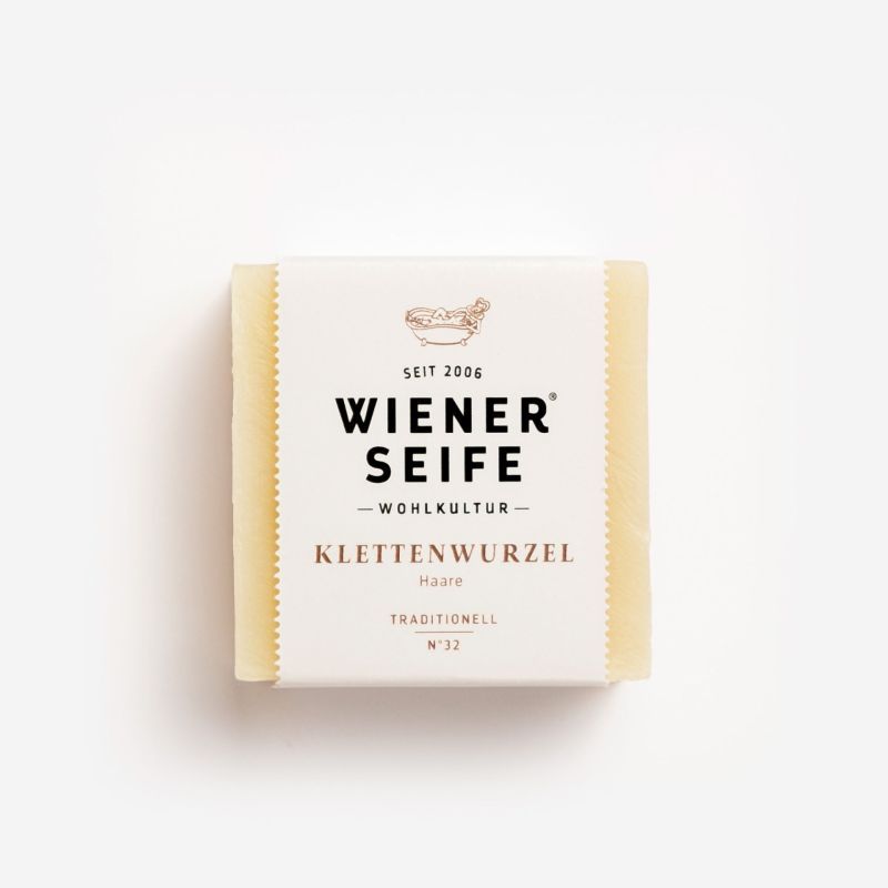 Seife mit Papierverpackung. Aufschrift: Wiener Seife, Klettenwurzel, Traditionell, N°32. Beige Seife, weißes Papier.