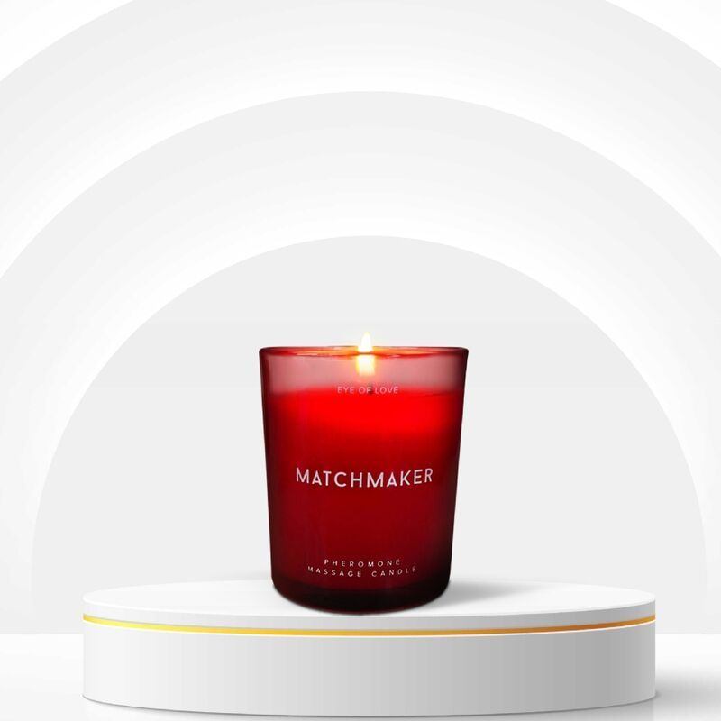 Rote Kerze im Glas auf Podest. Aufschrift: MATCHMAKER, EYE OF LOVE, Pheromone Massage Candle. Brennende Flamme.