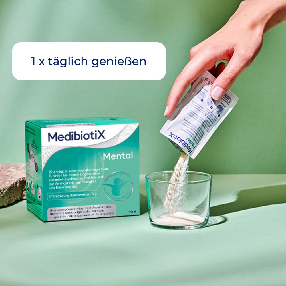 Hand gießt Pulver aus MedibiotiX Mental Beutel in Glas. Daneben Schachtel MedibiotiX Mental.
