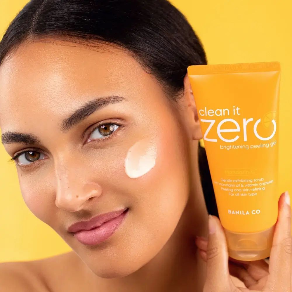 Orange Tube mit "clean it zero brightening peeling gel" Aufschrift. Weiße Creme auf Wange.