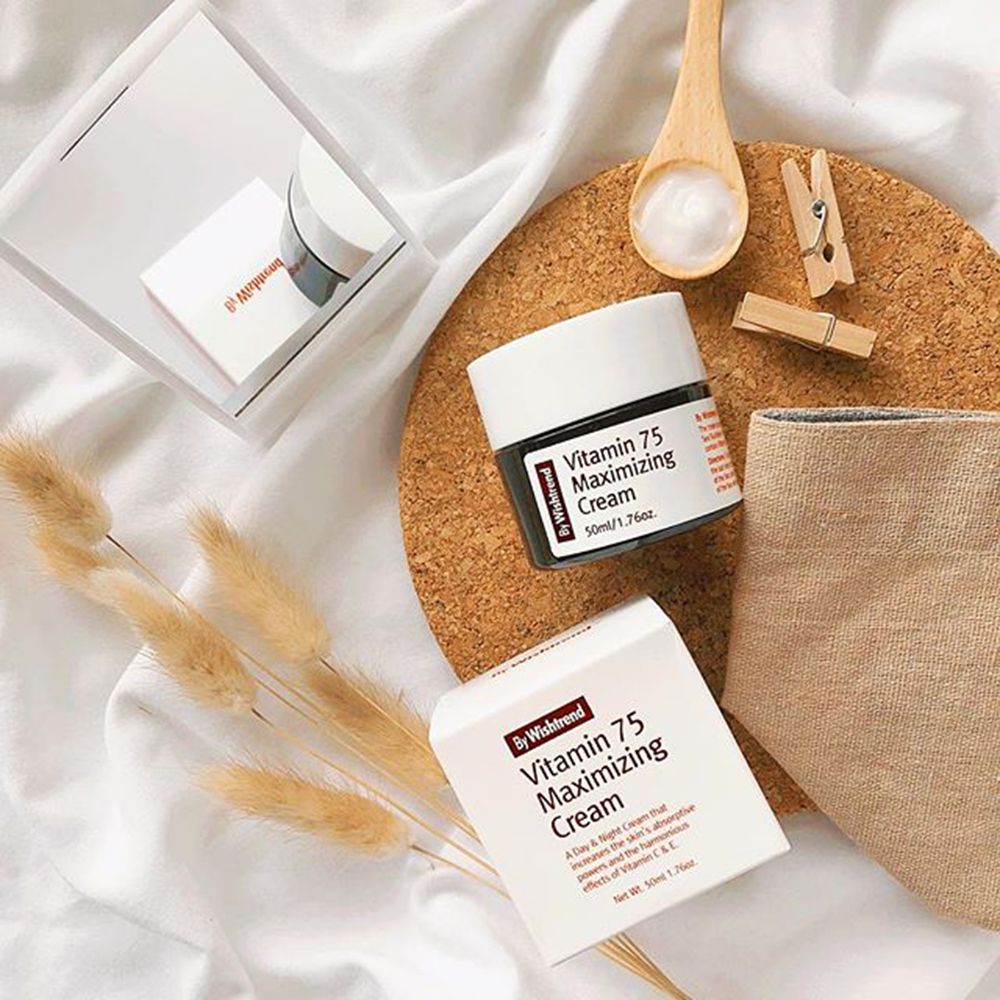 Produkt auf Korkplatte mit Zubehör. Glas und Schachtel mit roter Schrift: Vitamin 75 Maximizing Cream. Marke: By Wishtrend. Trockenblumen, Löffel, Klammer.