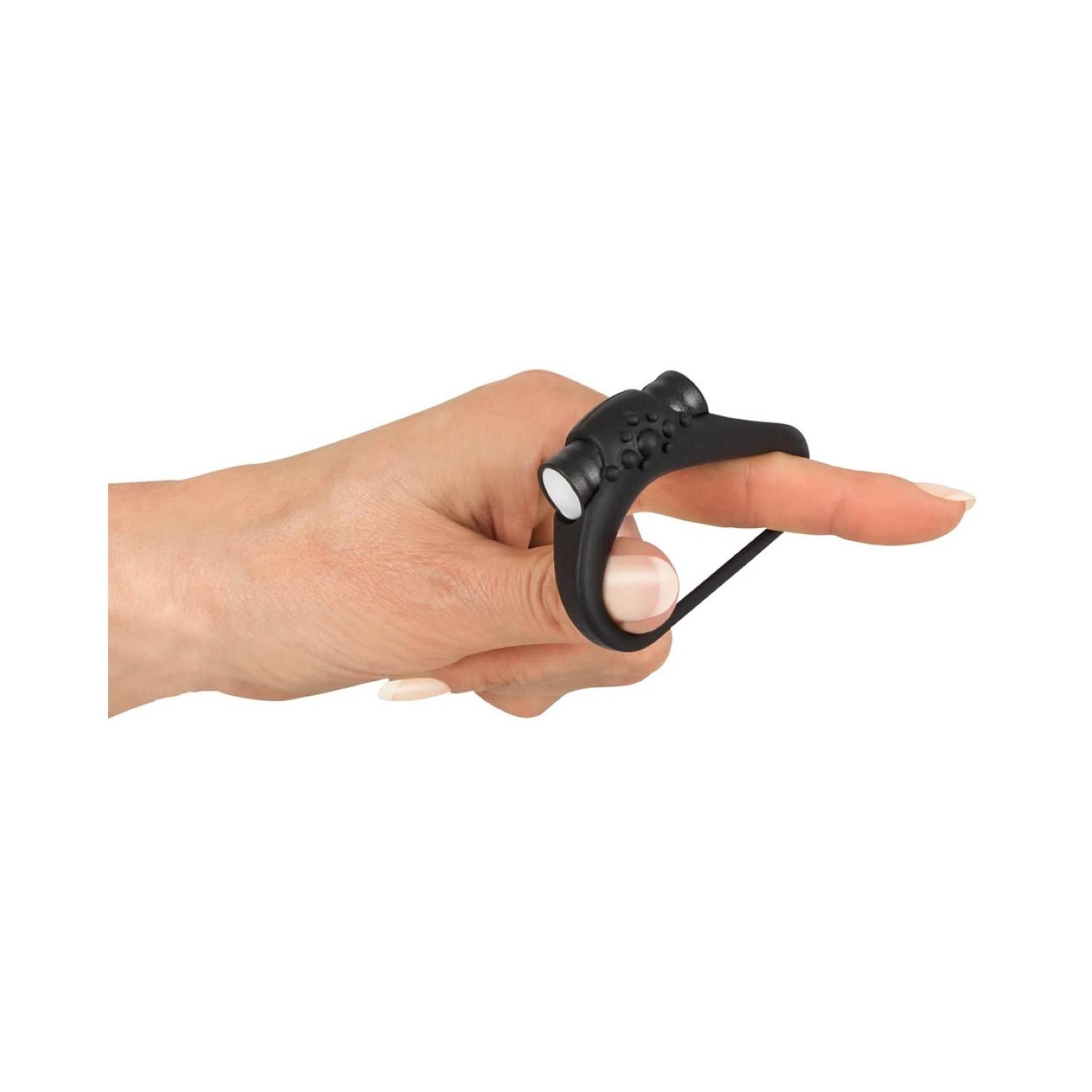Schwarzer Penisring auf einem Finger. Ring mit Noppen und zwei weißen Elementen.