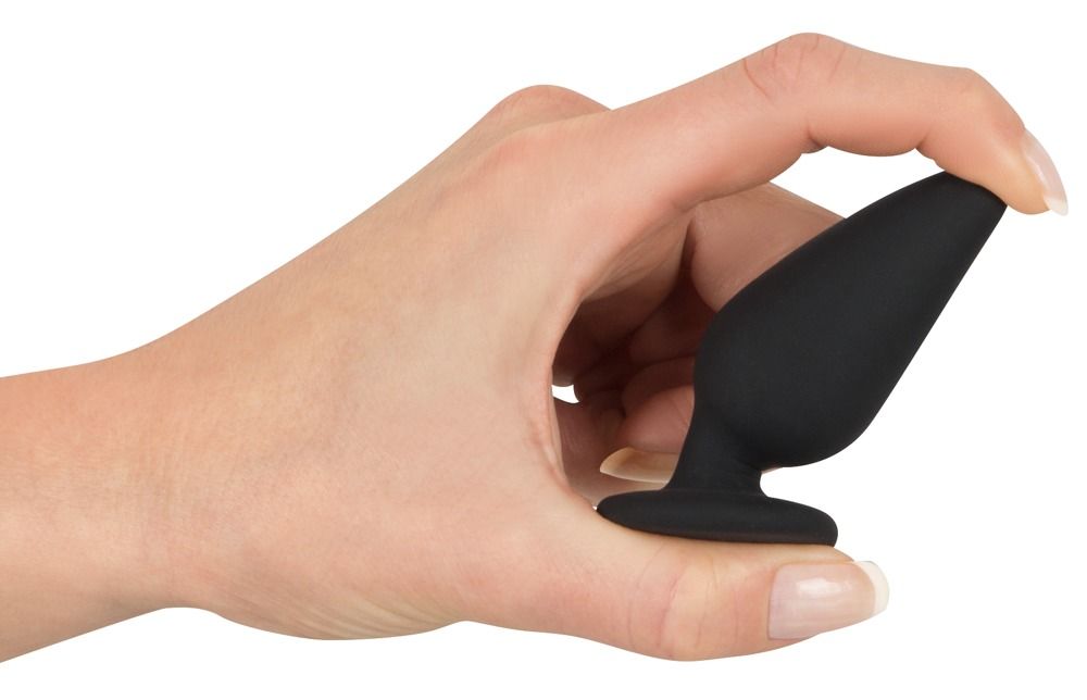Hand hält schwarzen Analplug. Konische Form, flacher Standfuß. Hautfarbe.