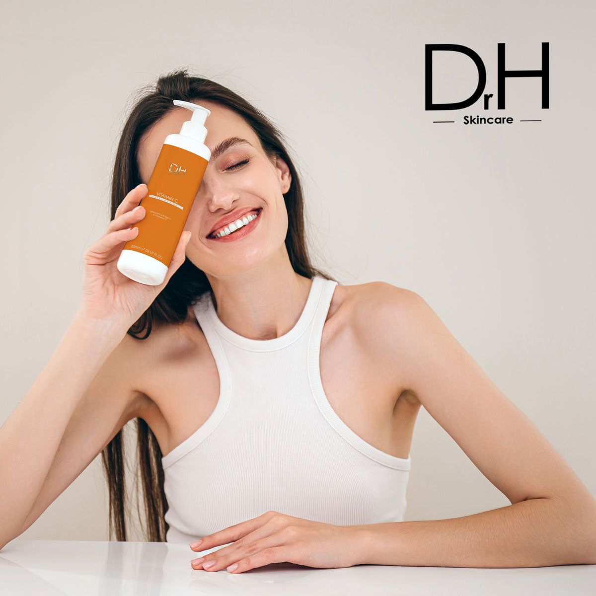 Frau hält Flasche vor dem Gesicht. Aufschrift: D.H. Skincare. Flasche: D.H. Vitamin C Anti-Aging. Weiße Schrift auf orangefarbenem Hintergrund.