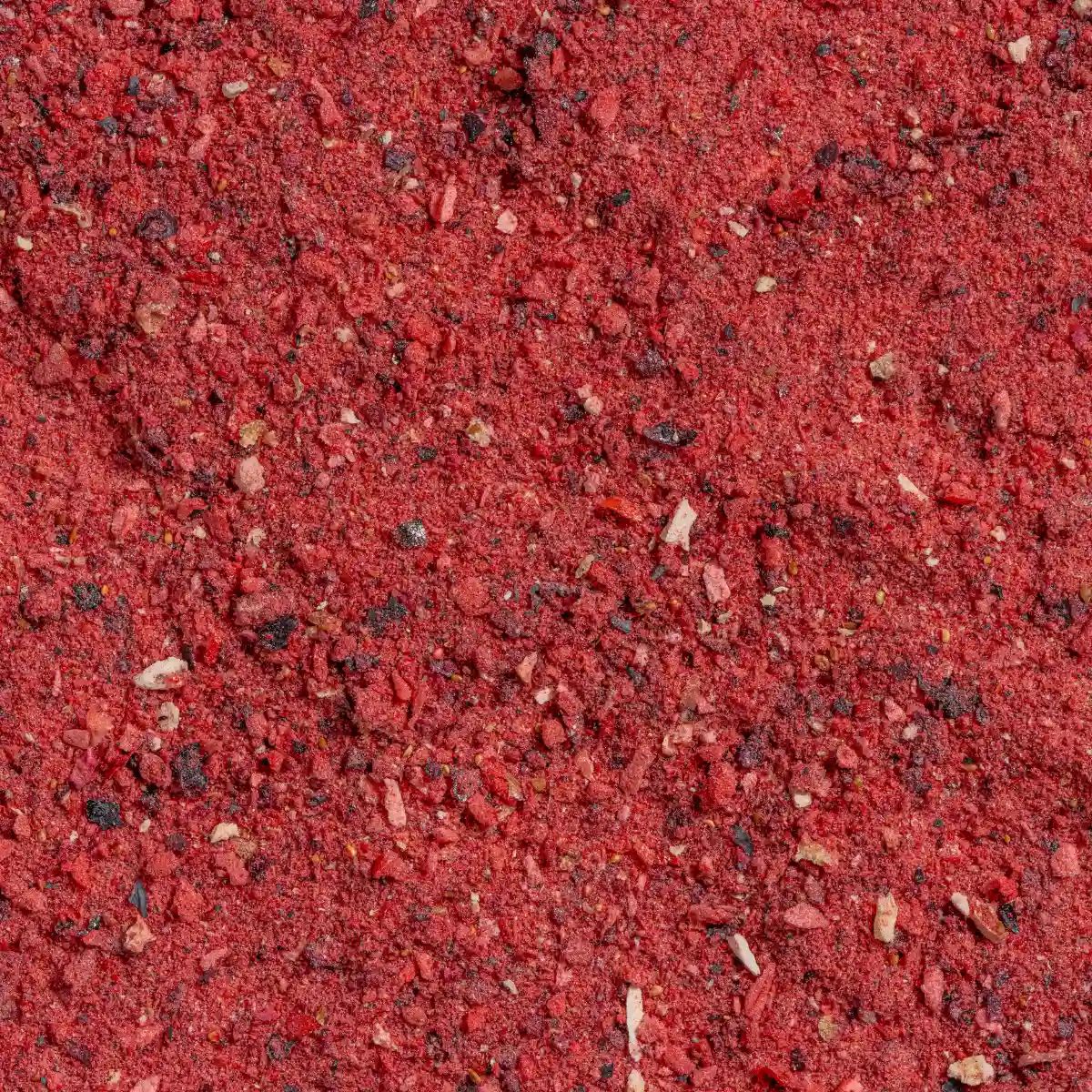 Nahaufnahme von rotem Fruchtpulver. Die Textur ist körnig und unregelmäßig, mit kleinen dunklen Partikeln.