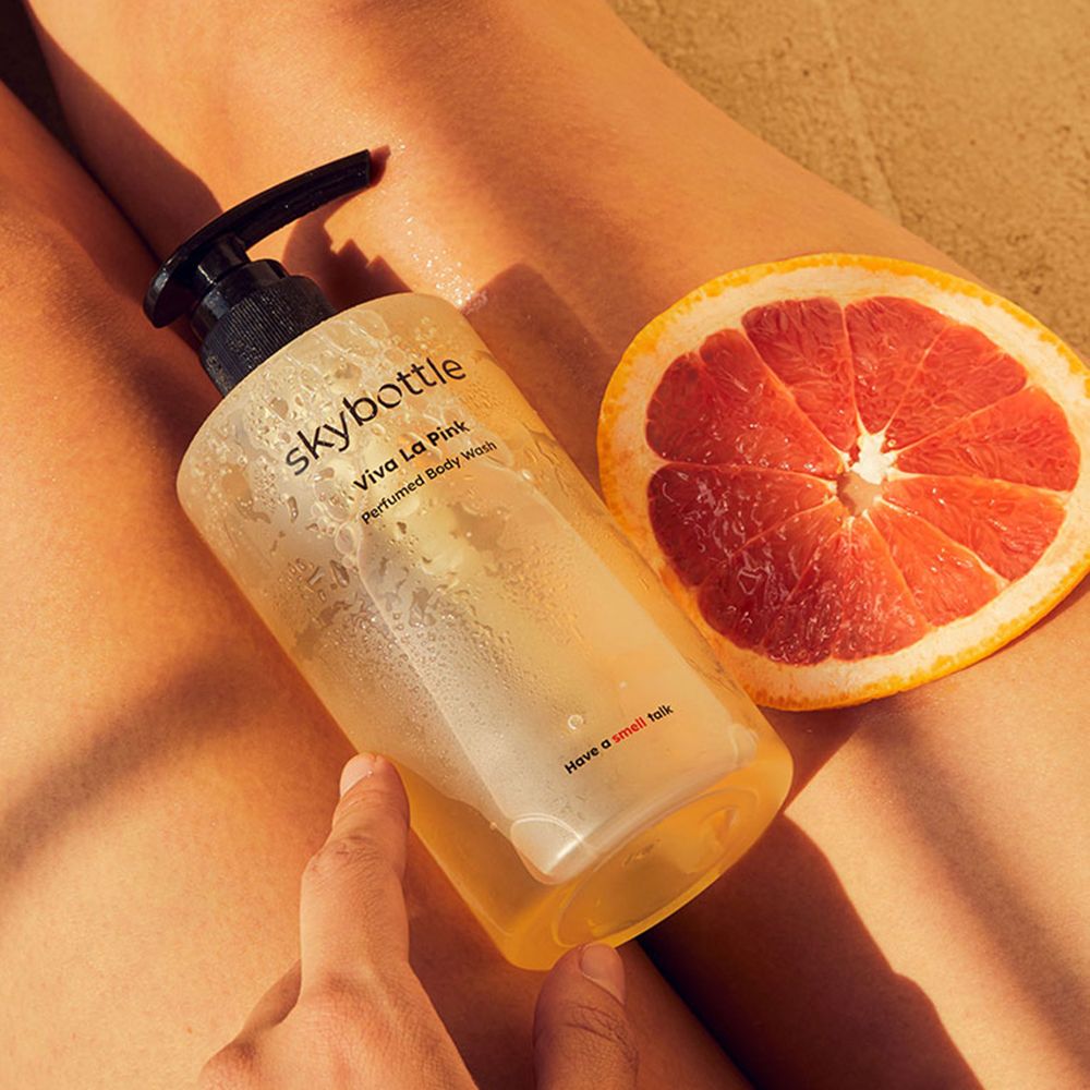 SKYBOTTLE Viva La Pink Duschgel-Flasche und Grapefruit-Hälfte auf Beinen. Schwarzer Spender. Text: Viva La Pink, Perfumed Body Wash.