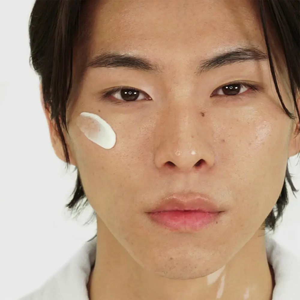 Nahaufnahme eines Mannes. Auf der Wange ist eine weiße Creme aufgetragen.