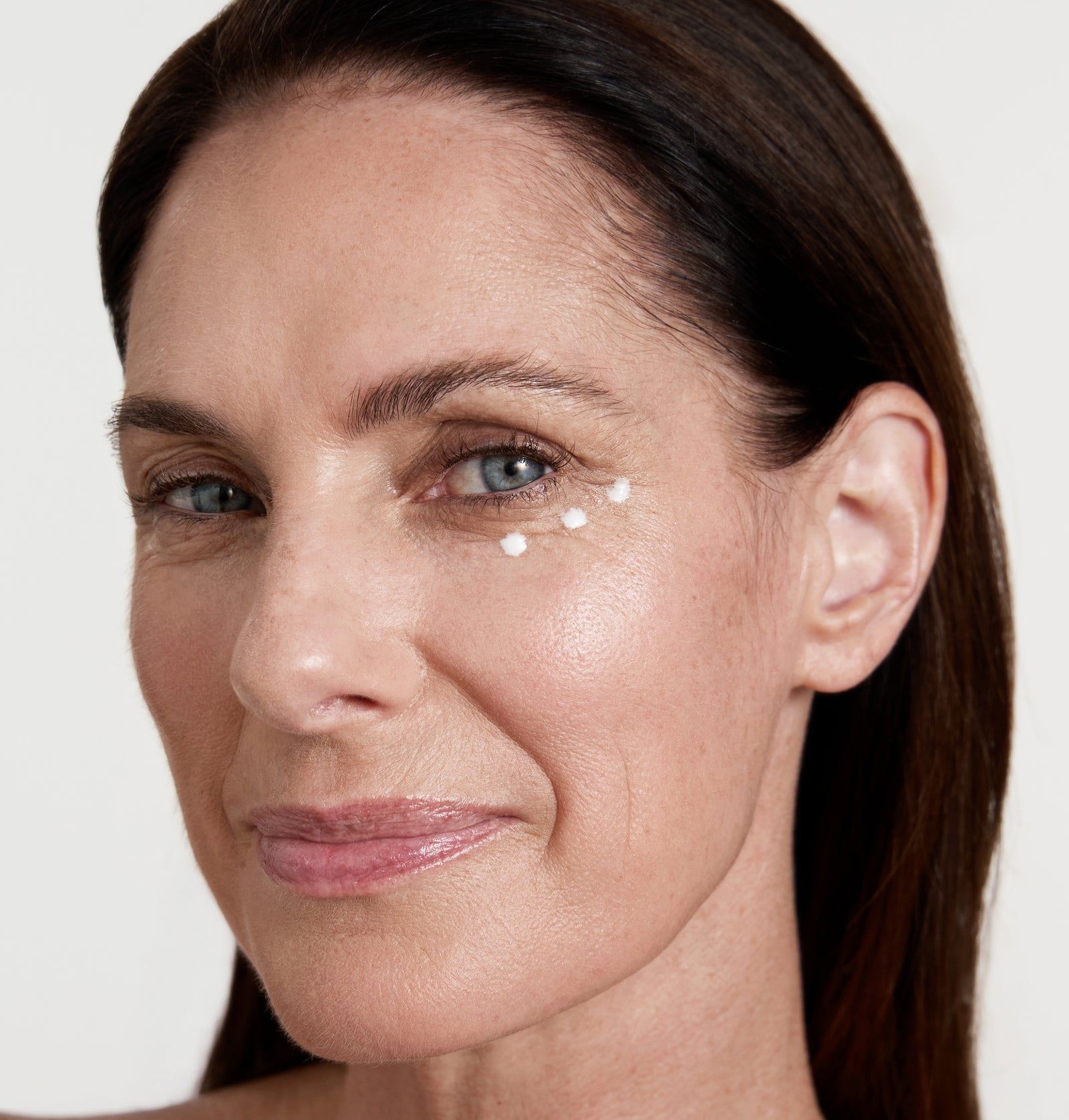 Frau mit Produktpunkten unter dem Auge. Helle Haut, braunes Haar. Produkt auf der Haut sichtbar.