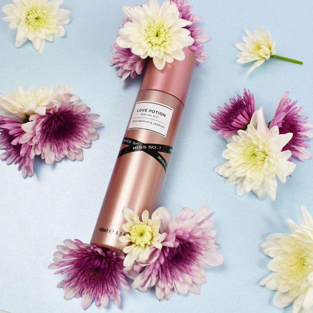 Rosa Körperspray 'Love Potion' umgeben von Blumen. Marke: Miss So...?