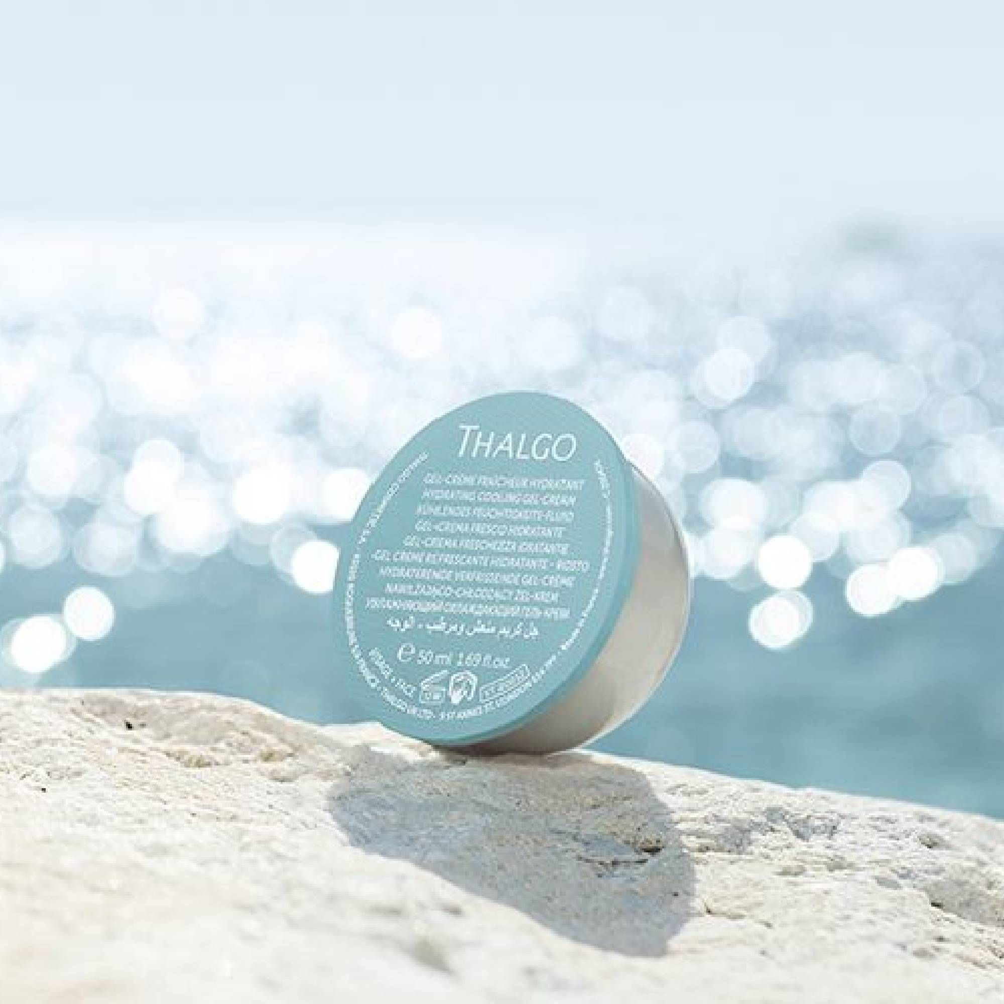 Kühlendes Feuchtigkeitsfluid-Behälter auf Felsen am Meer. Weißer, runder Behälter mit blauem Deckel. Text: THALGO, Gel-Creme Fraîcheur Hydratant.