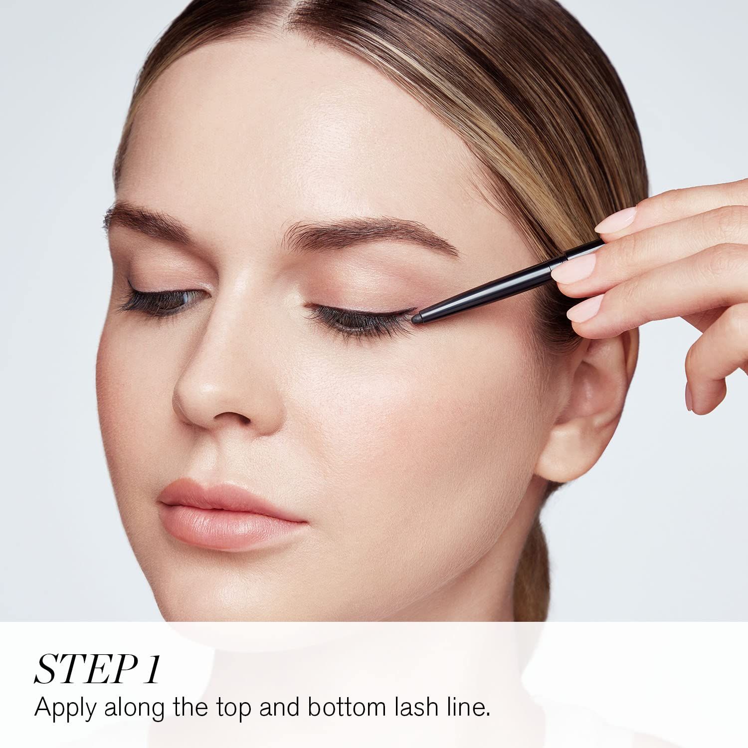 Frau trägt Eyeliner auf. Nahaufnahme einer Frau, die Eyeliner auf das obere Augenlid aufträgt. Text: STEP 1.
