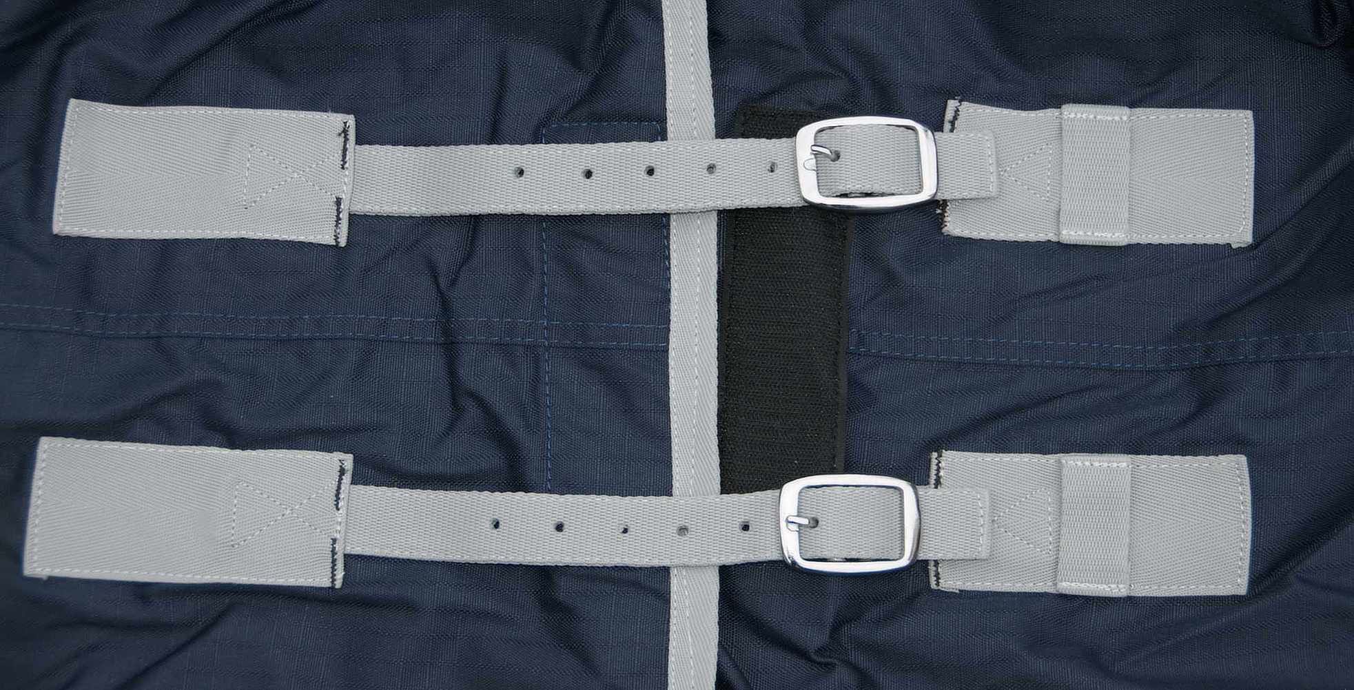 Nahaufnahme der Unterseite der Pferdedecke. Zwei graue Gurte mit silbernen Schnallen. Dunkelblauer Stoff.