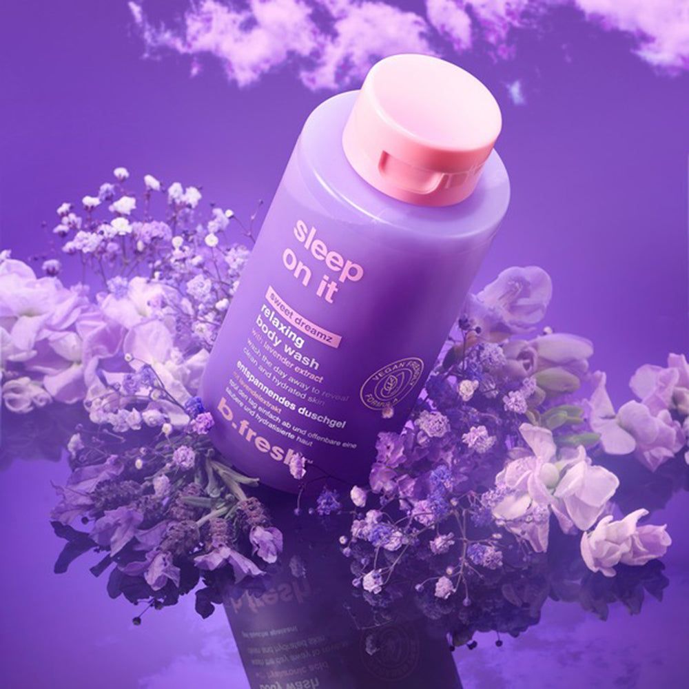 Lila Duschgel-Flasche mit rosa Deckel, schräg auf lila Blumen. Aufschrift: Sleep On It, Relaxing Body Wash, b.fresh. Vegan-Siegel.