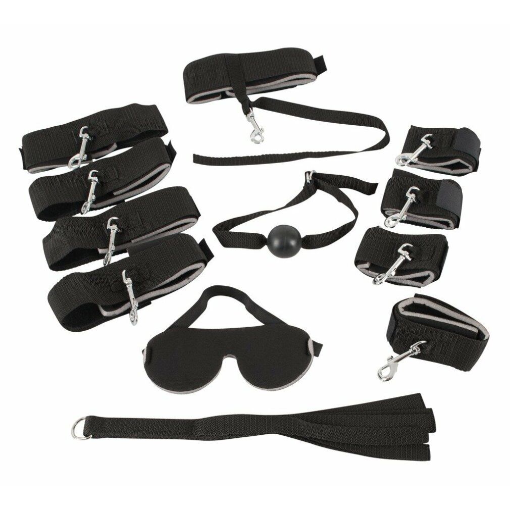Zubehör-Set: Augenmaske, Fesseln, Knebel, Peitsche. Schwarzes Material mit Metallringen und Verschlüssen. Draufsicht.