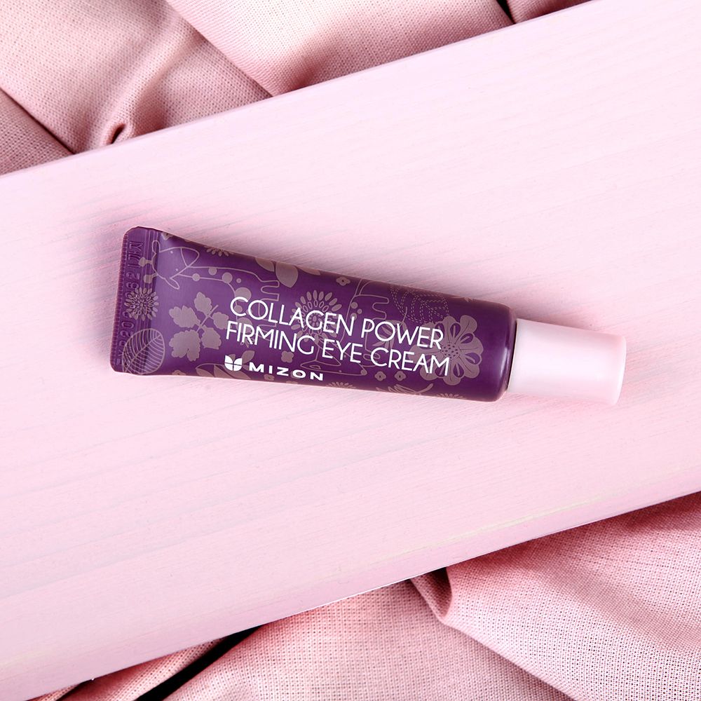 Lila Tube MIZON Collagen Power Firming Eye Cream auf rosa Stoff. Rosa Kappe. Text: Collagen Power Firming Eye Cream.