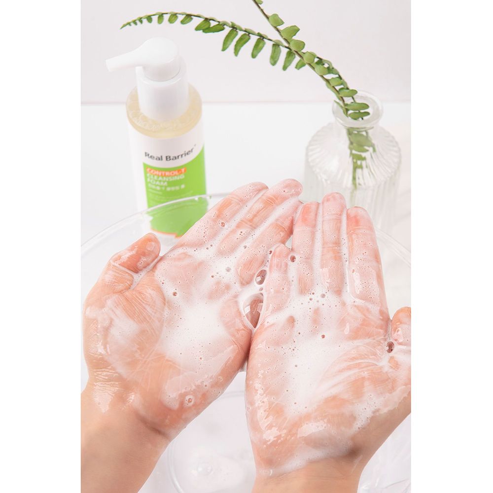 Hände mit Schaum. Flasche Real Barrier Control-T Cleansing Foam im Hintergrund.