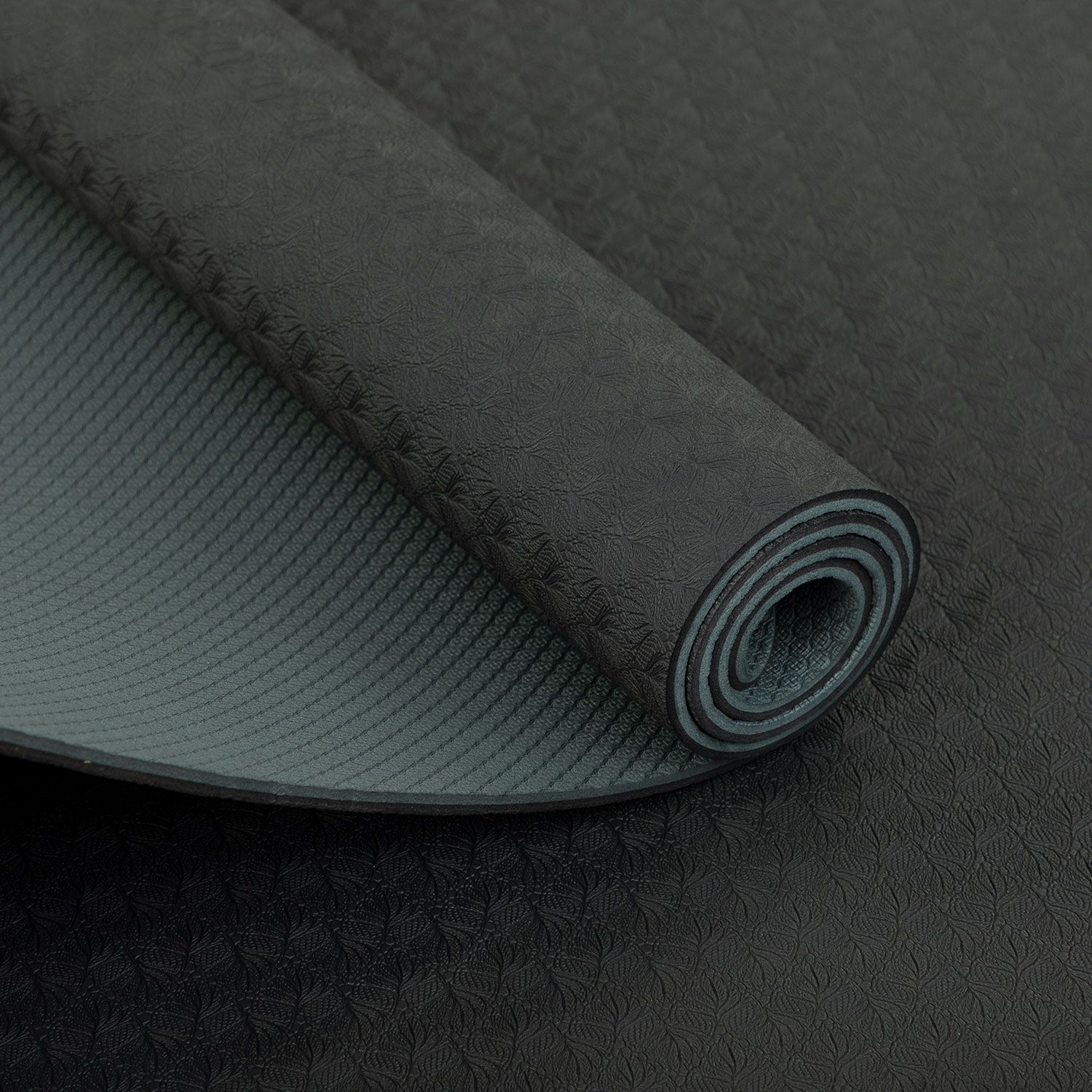 Yogamatte, aufgerollt. Anthrazitfarbene Oberseite mit Muster, graue Unterseite. Detailansicht.
