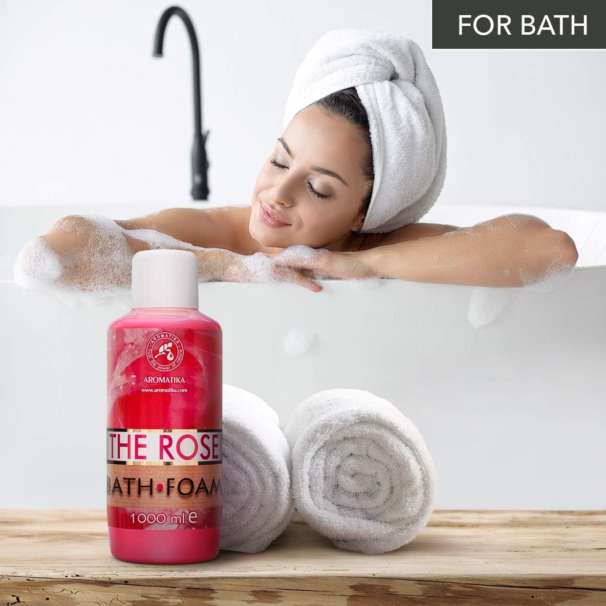 Rosa Flasche AROMATIKA THE ROSE BATH FOAM neben einer Badewanne. Frau mit Handtuch auf dem Kopf entspannt sich im Bad.