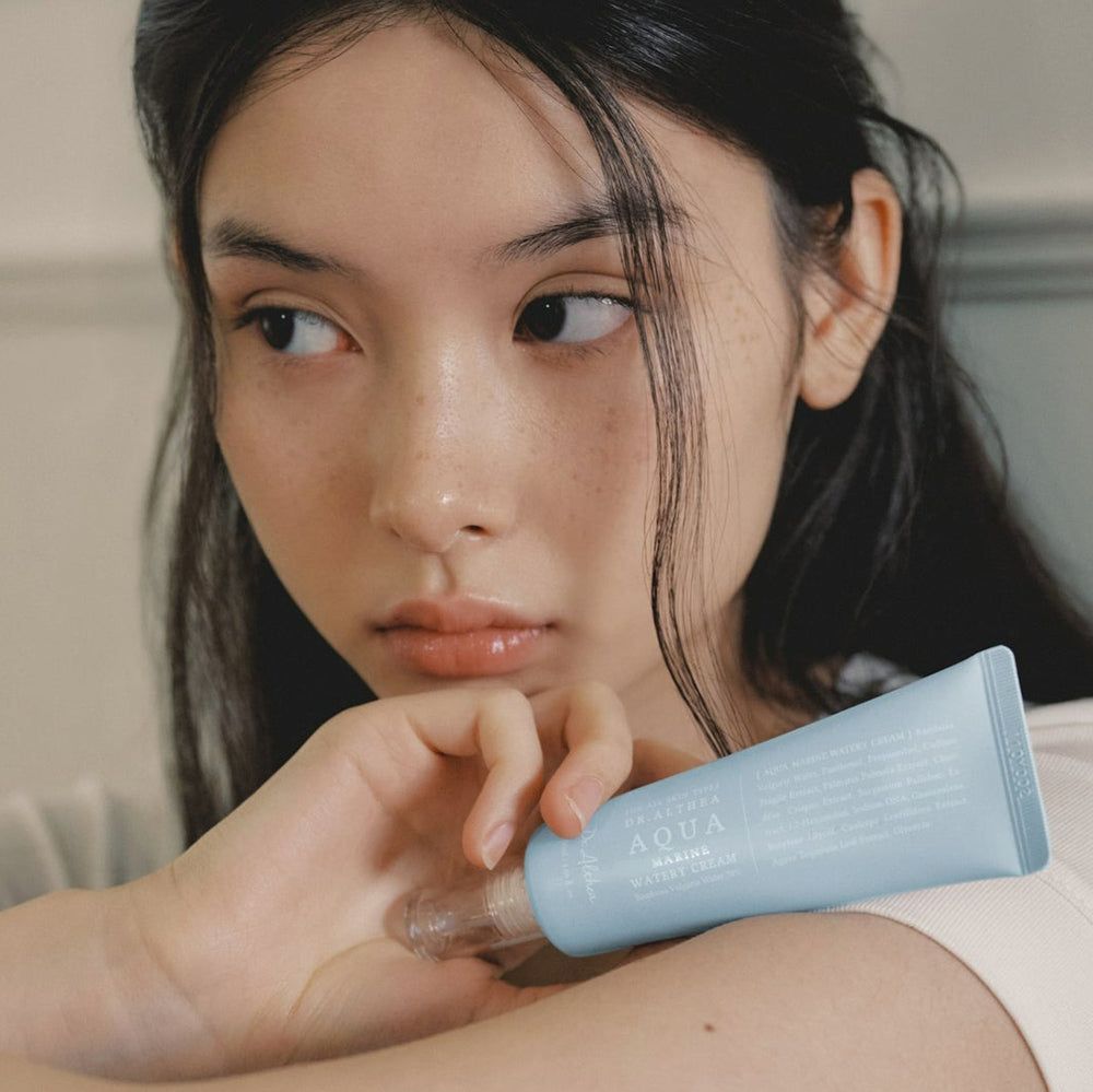 Eine Frau hält eine hellblaue Tube. Produktname: Aqua Marine Watery Cream. Marke: Dr. Althea. Transparenter Applikator.