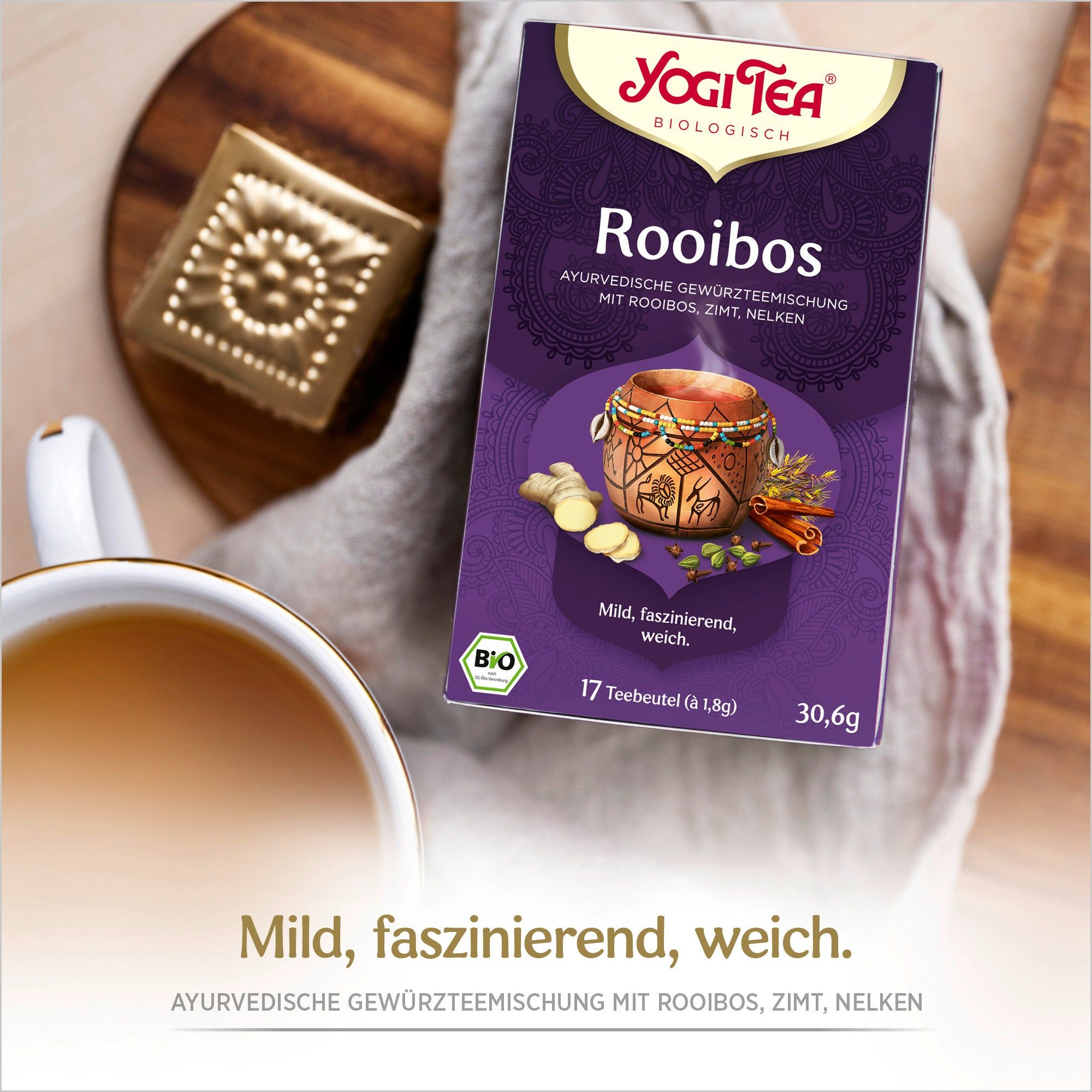 Yogi Tea Rooibos Bio Gewürztee-Packung. Lila Verpackung mit Logo und Produktbezeichnung. Bio-Siegel. Auf Holzbrett.
