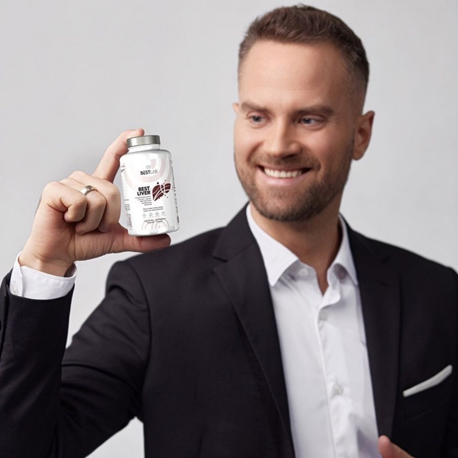 Mann hält eine Flasche BEST LAB BEST LIVER. Er lächelt und trägt einen Anzug.